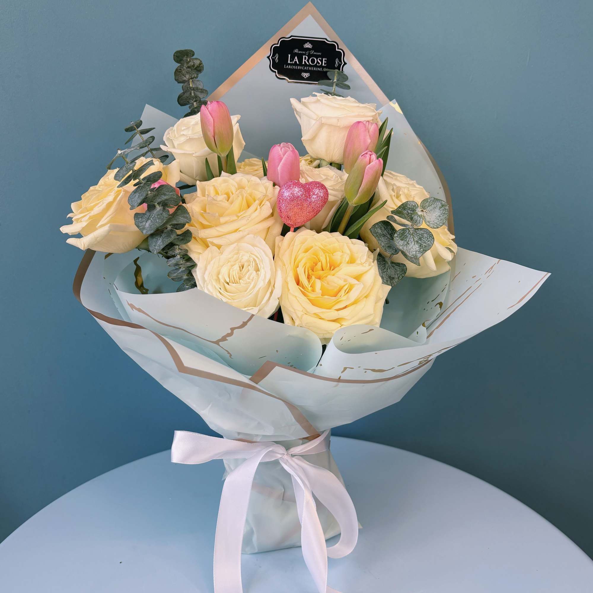 Bouquet of cream roses and pink tulips wrapped in white paper with a ribbon