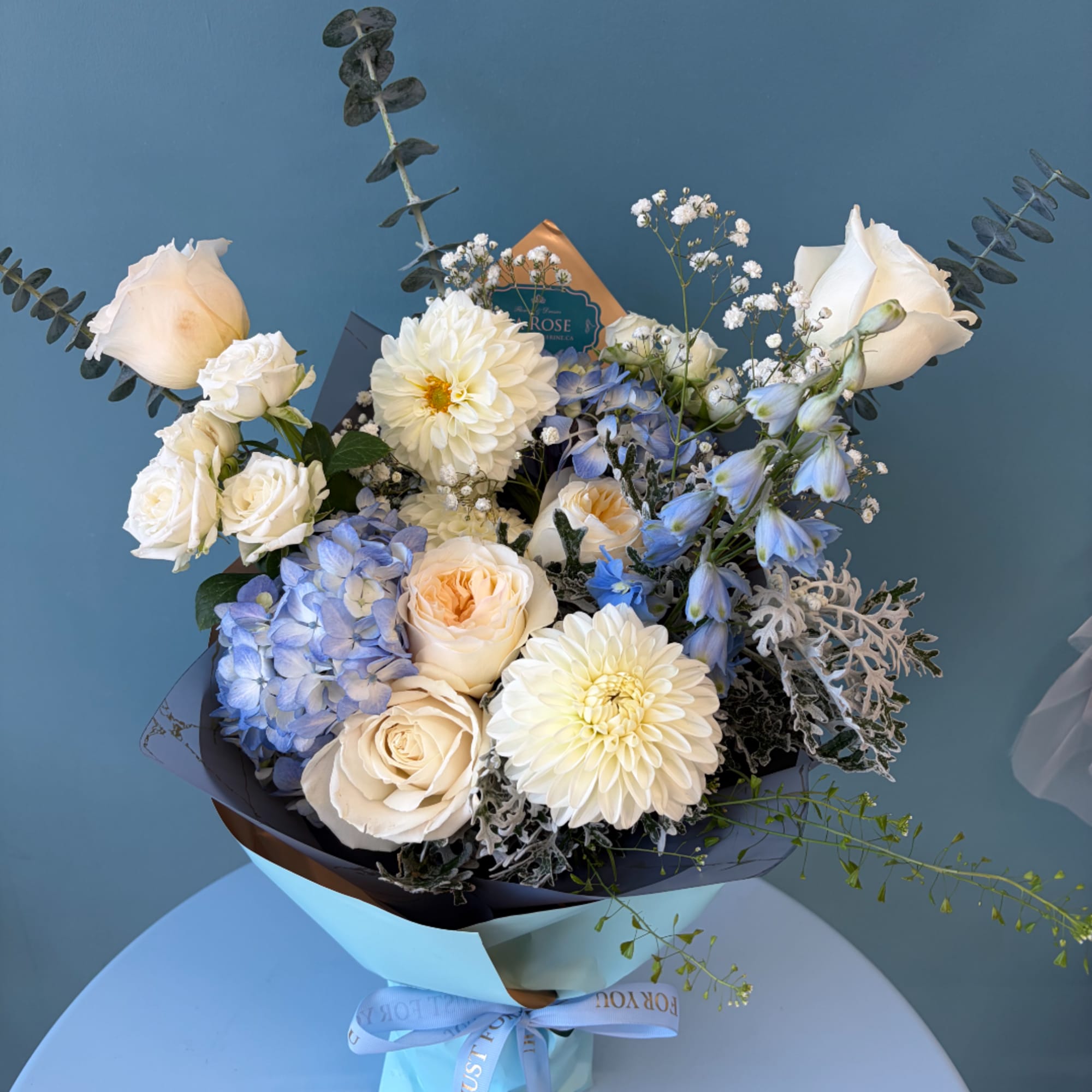 Bouquet of cream roses, white dahlias, and blue flowers in pastel wrapping