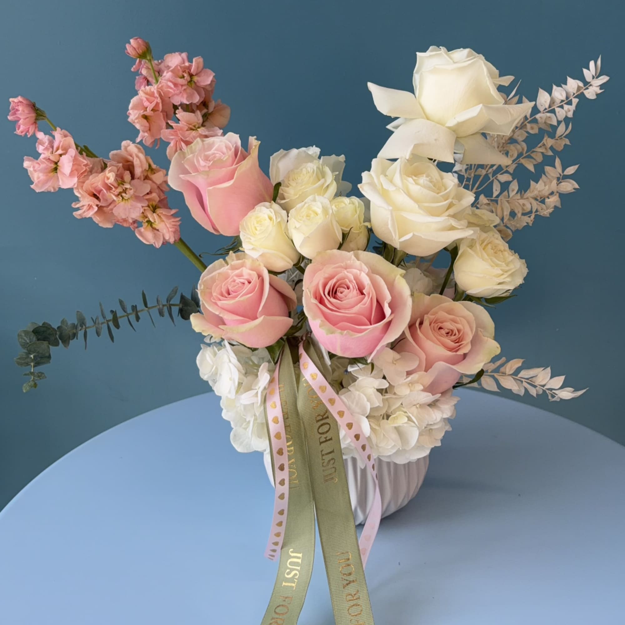 Pink and white roses in a white vase with ribbon