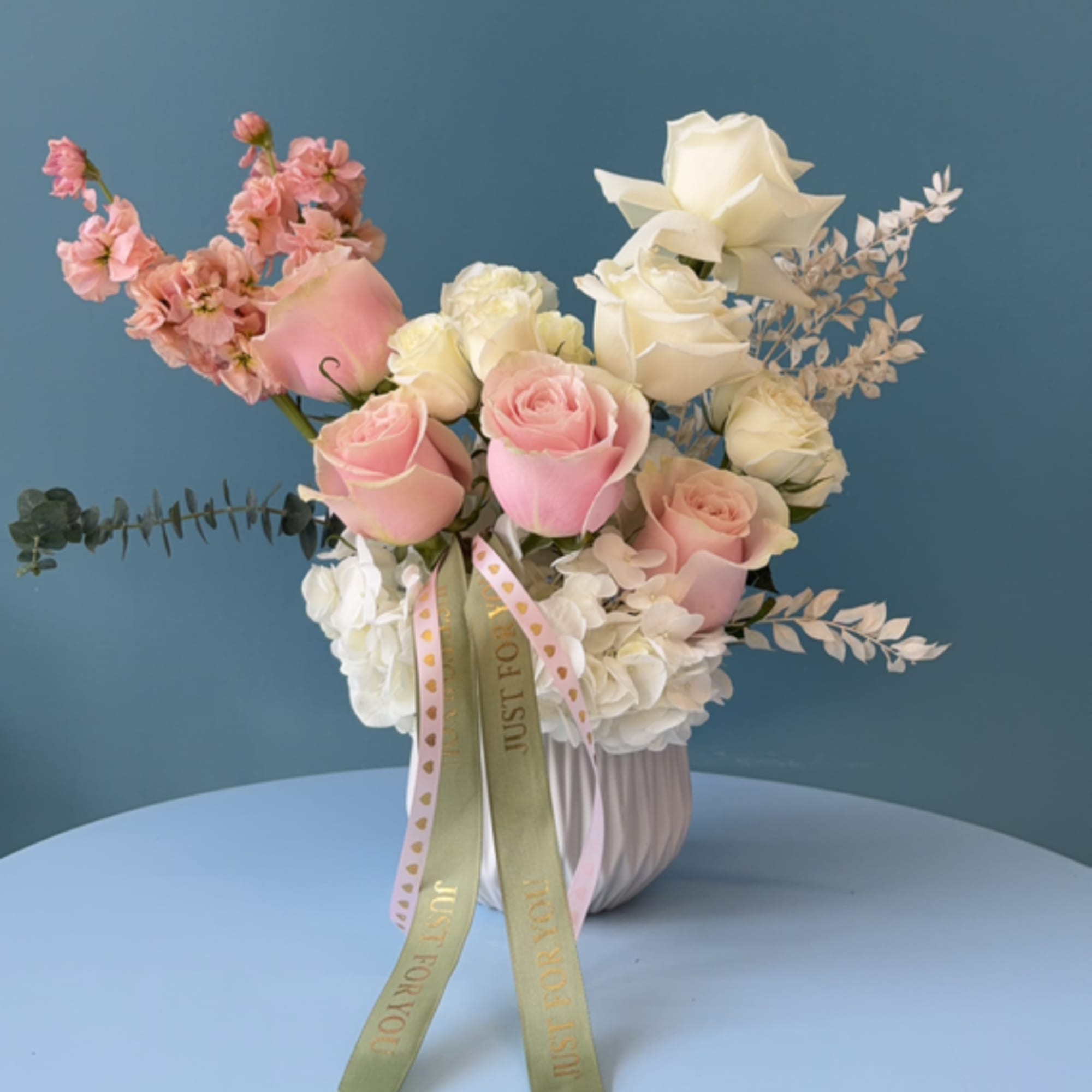 Pink and white roses arranged in a ribbed vase with ribbon