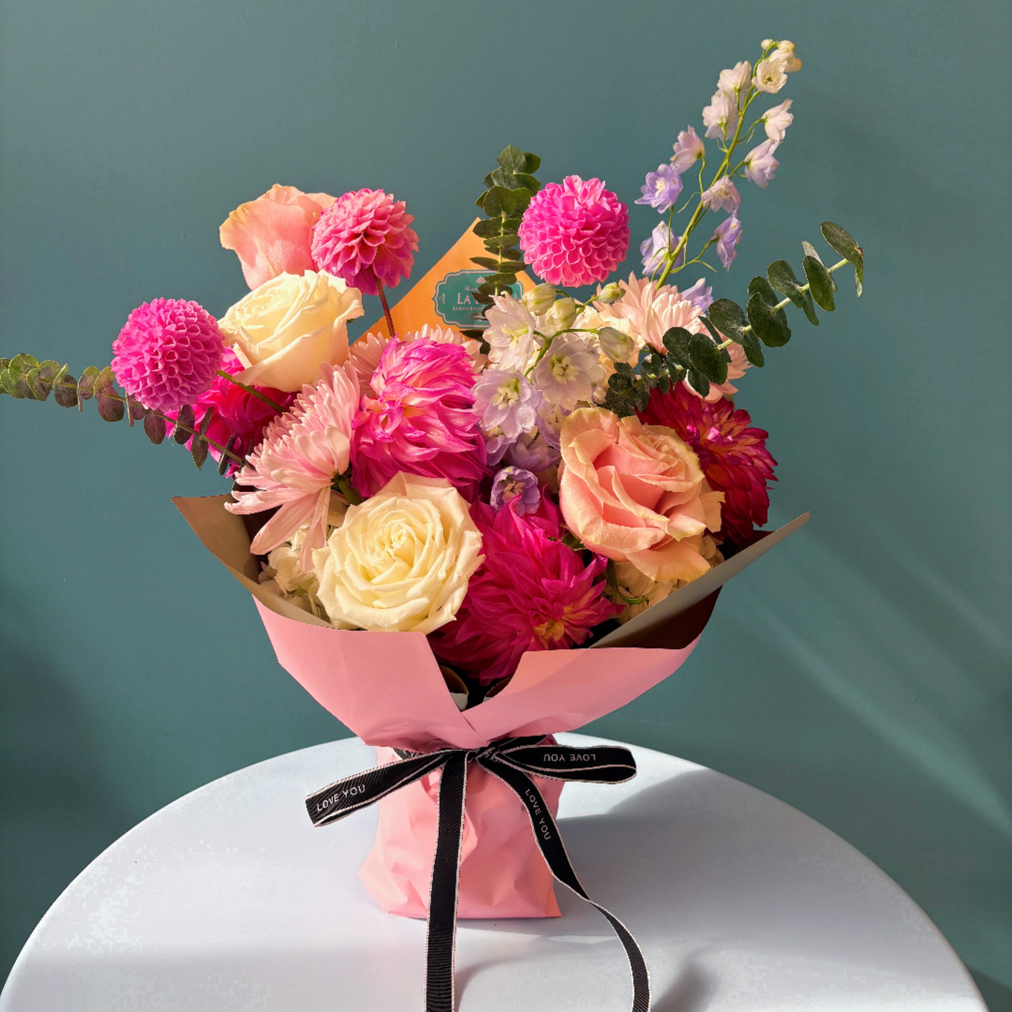 Pink and peach bouquet with roses, dahlias, and lavender blooms in pink wrap