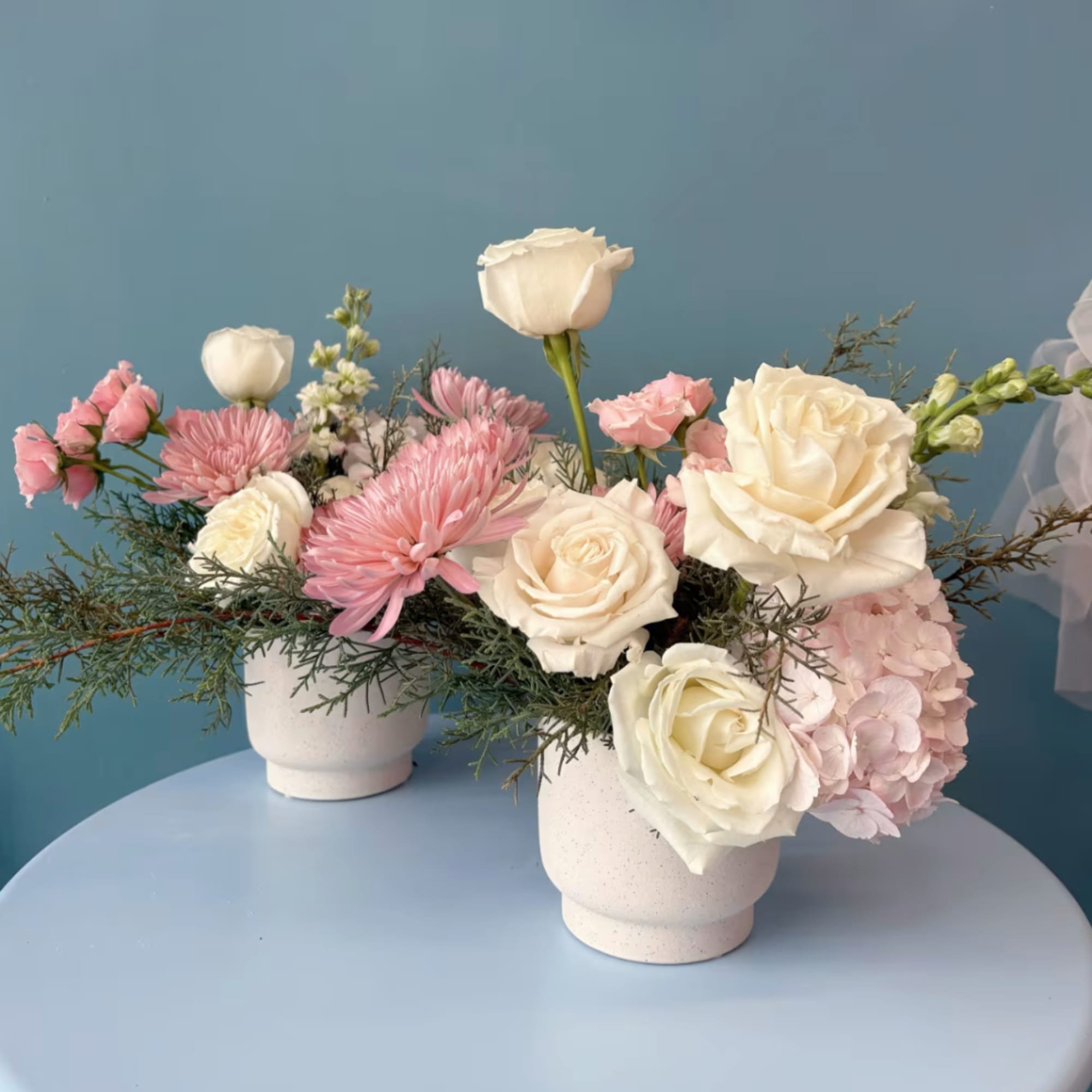 Pink and white floral arrangements in white pots on a blue table