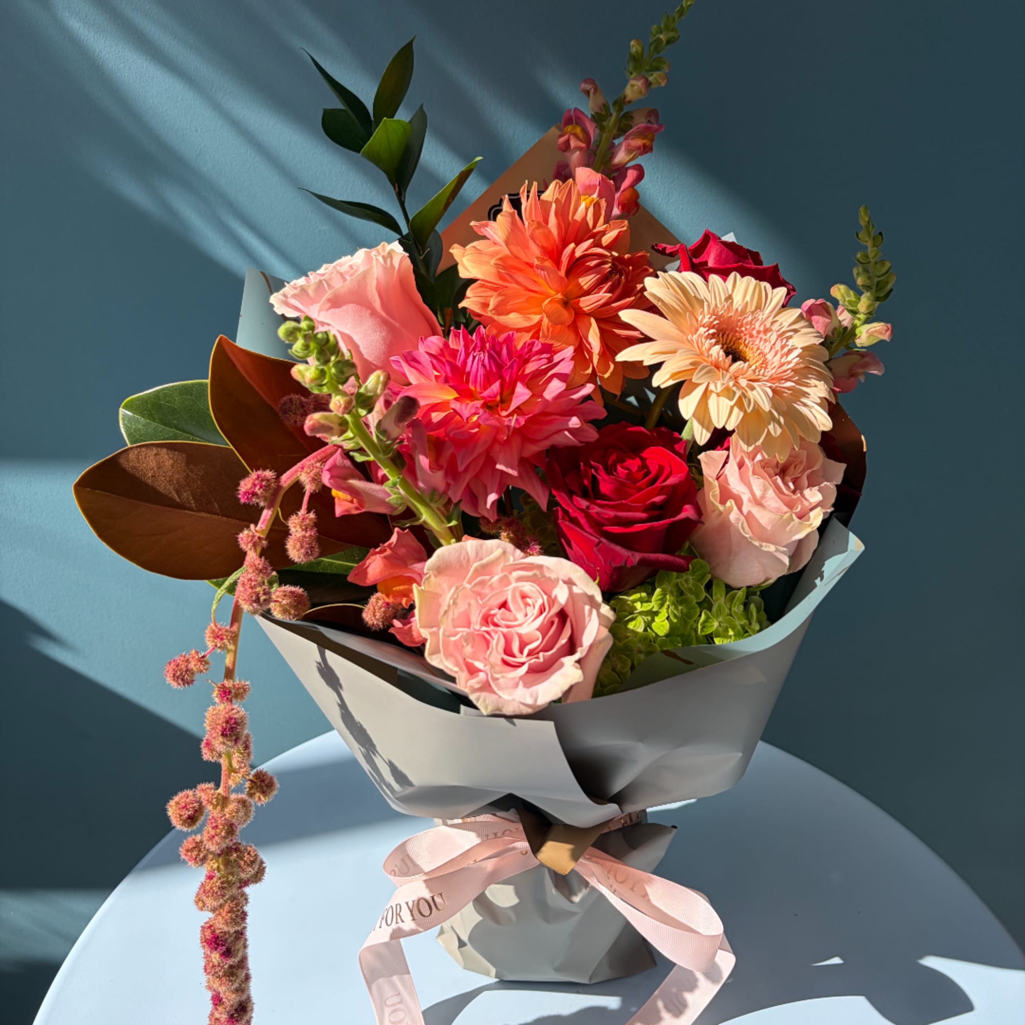 Bouquet of pink and orange flowers wrapped in gray paper with a pink ribbon
