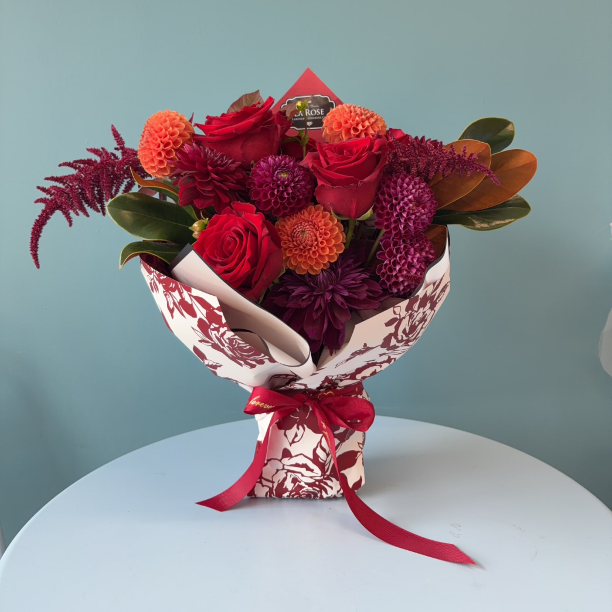 Bouquet of red roses and purple dahlias in patterned wrap with ribbon