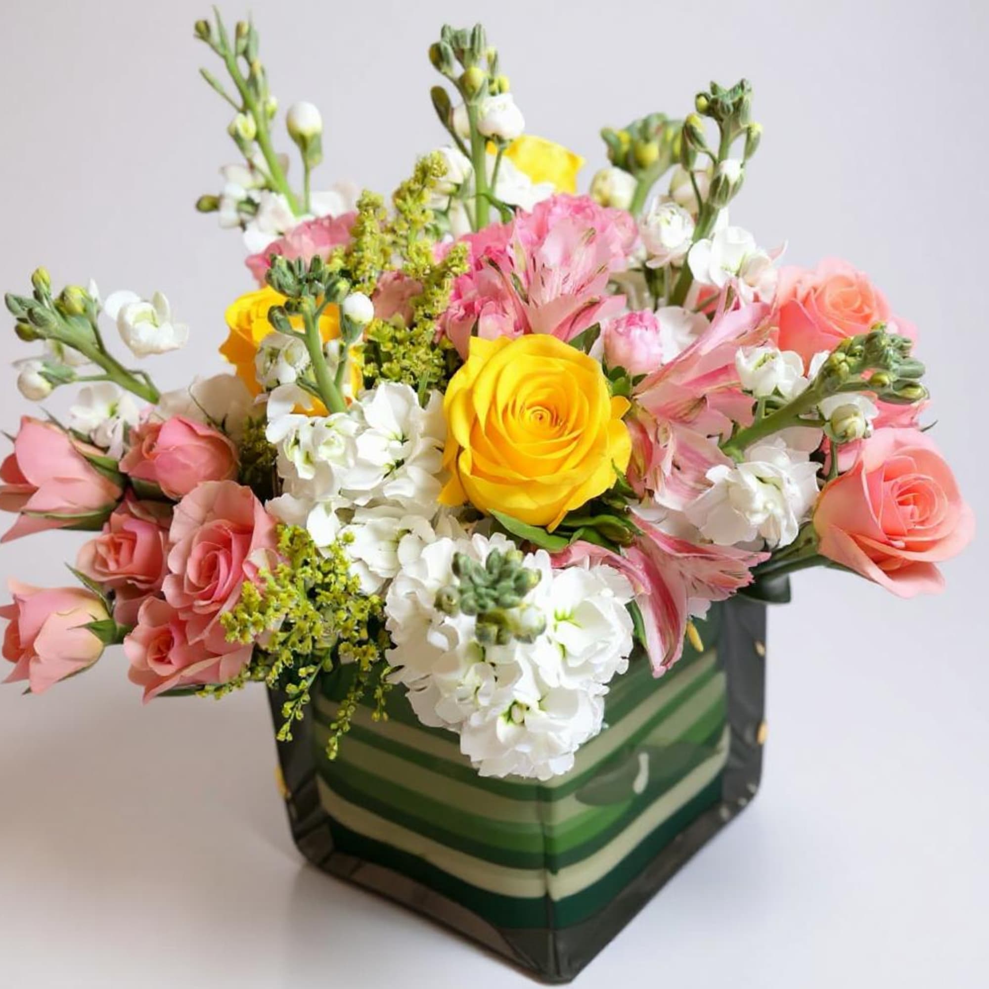 Mixed bouquet of pink, white, and yellow flowers in a striped square box