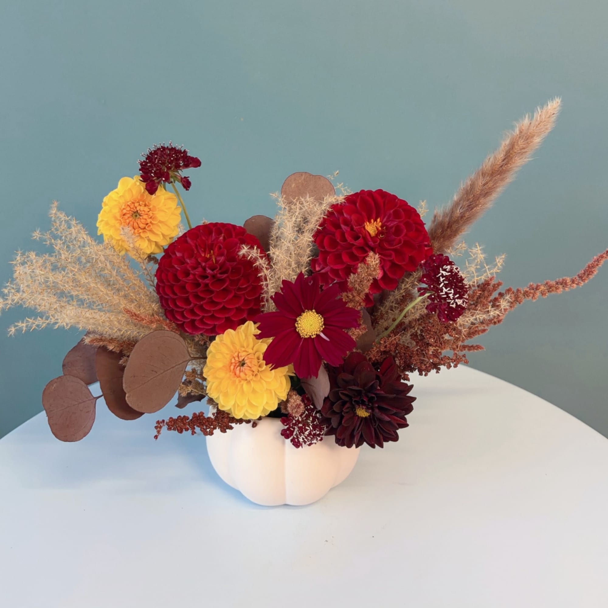 Mixed bouquet of red and yellow flowers in a white pumpkin vase