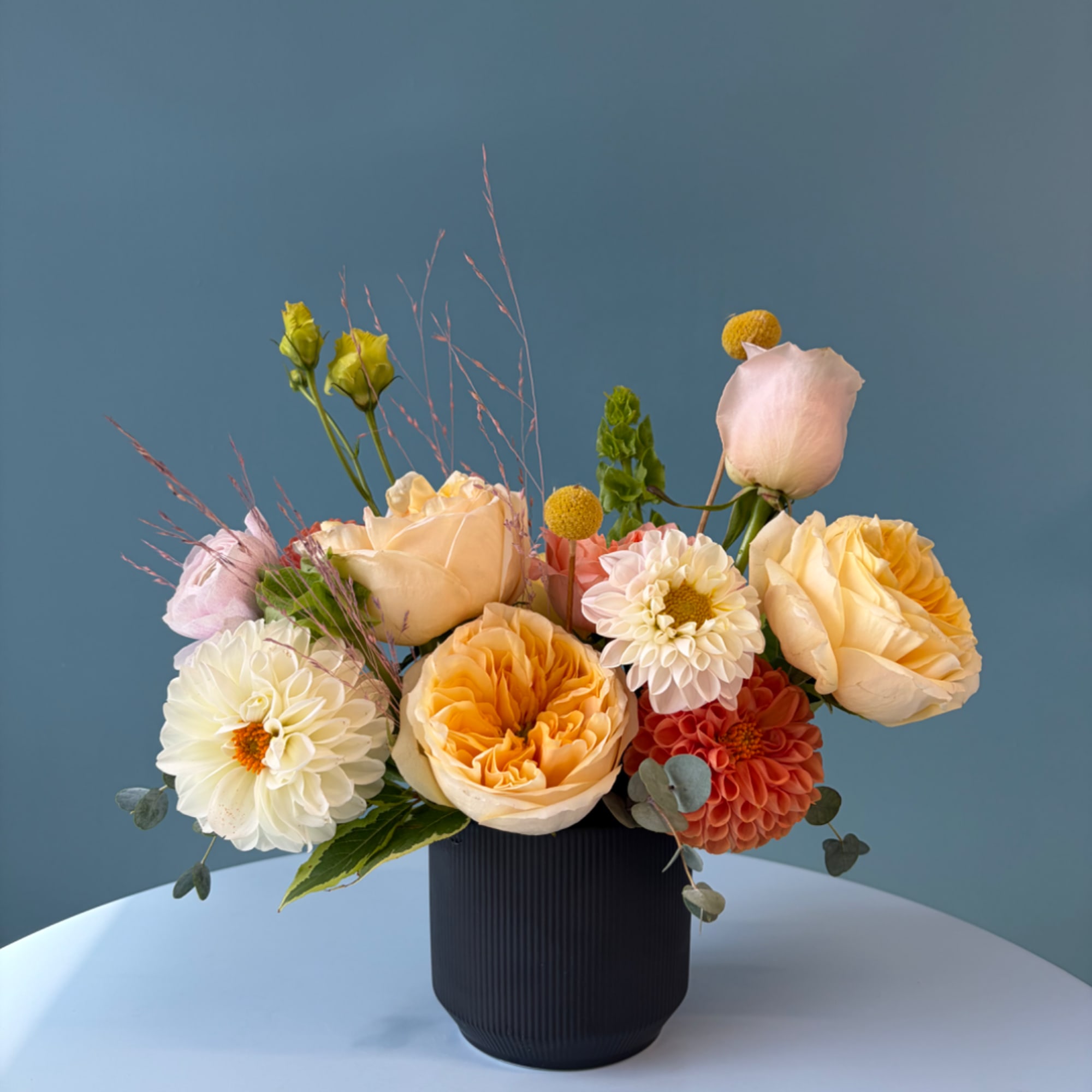 Mixed bouquet of peach, cream, and pink flowers in a black vase