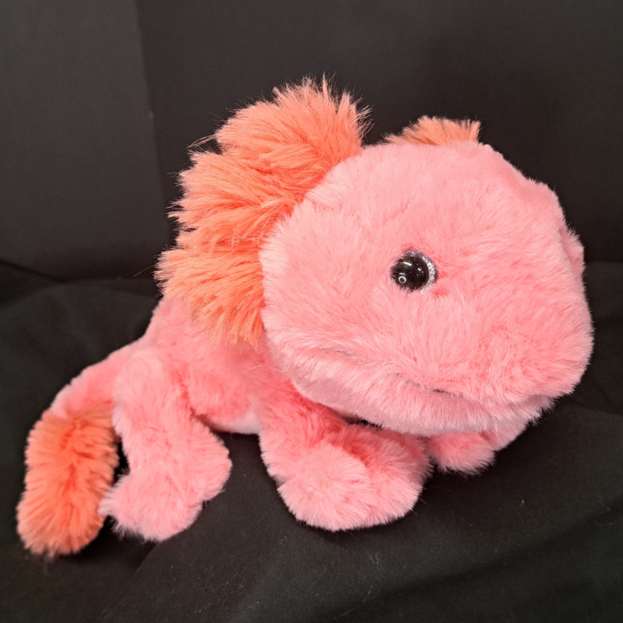 Pink plush stuffed animal with orange accents on a dark background