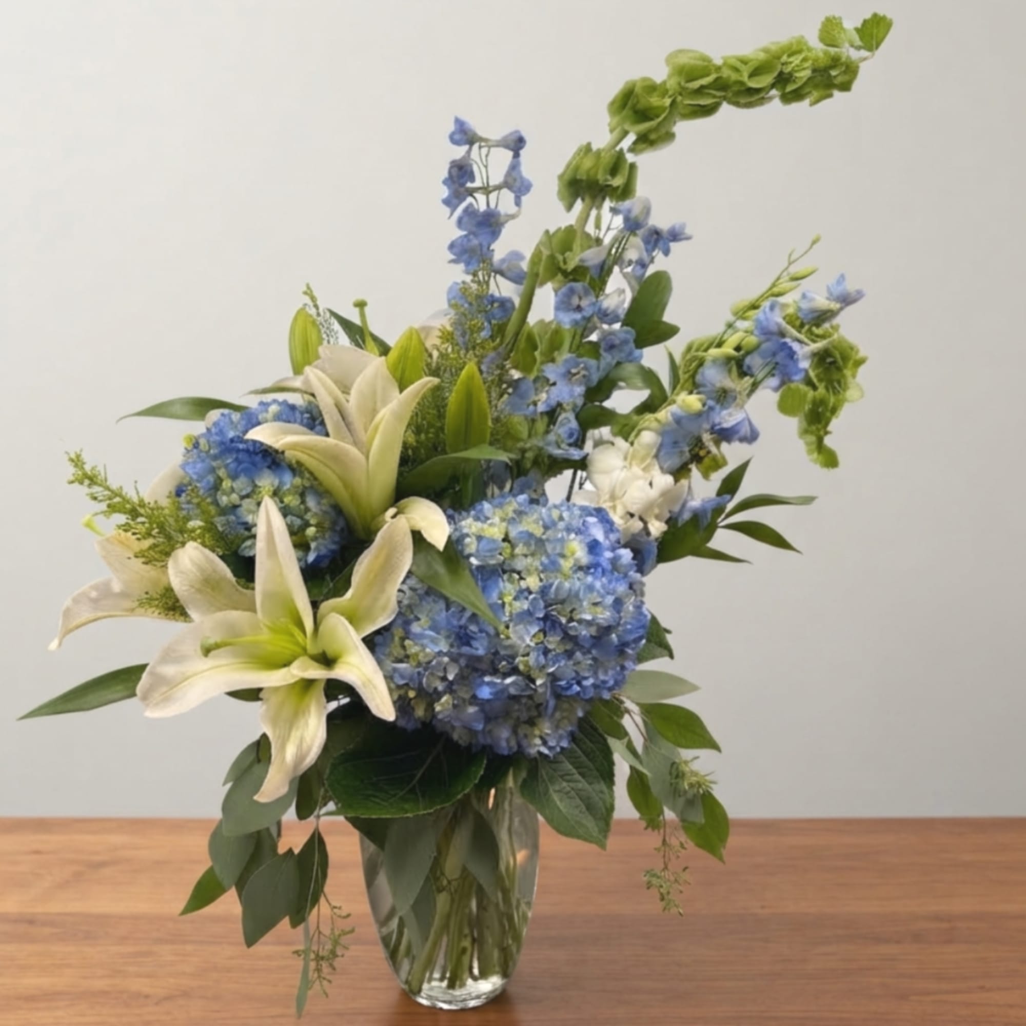 Blue hydrangeas and white lilies in a clear glass vase, photo 2 of 4