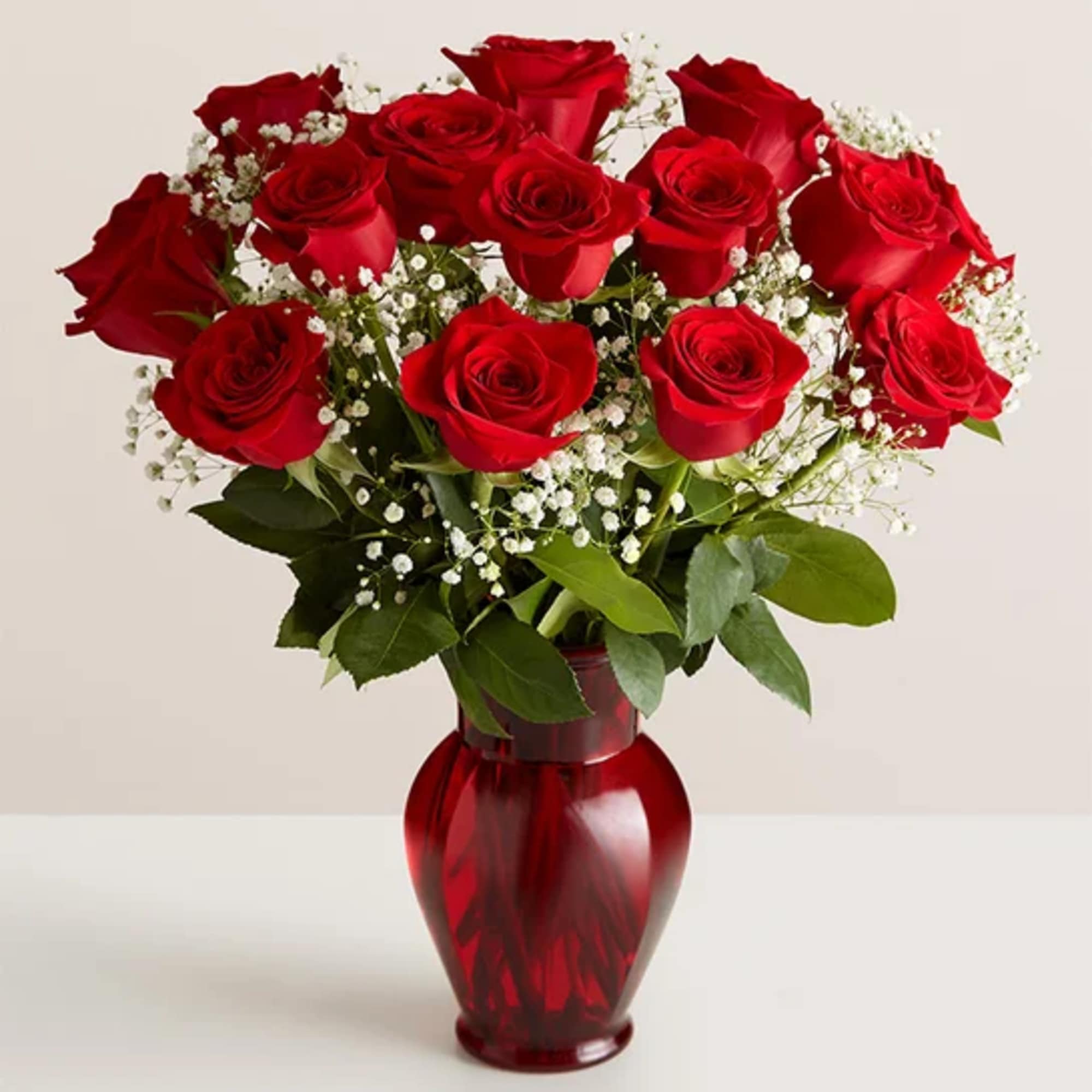 Red roses arranged in a red glass vase with baby's breath