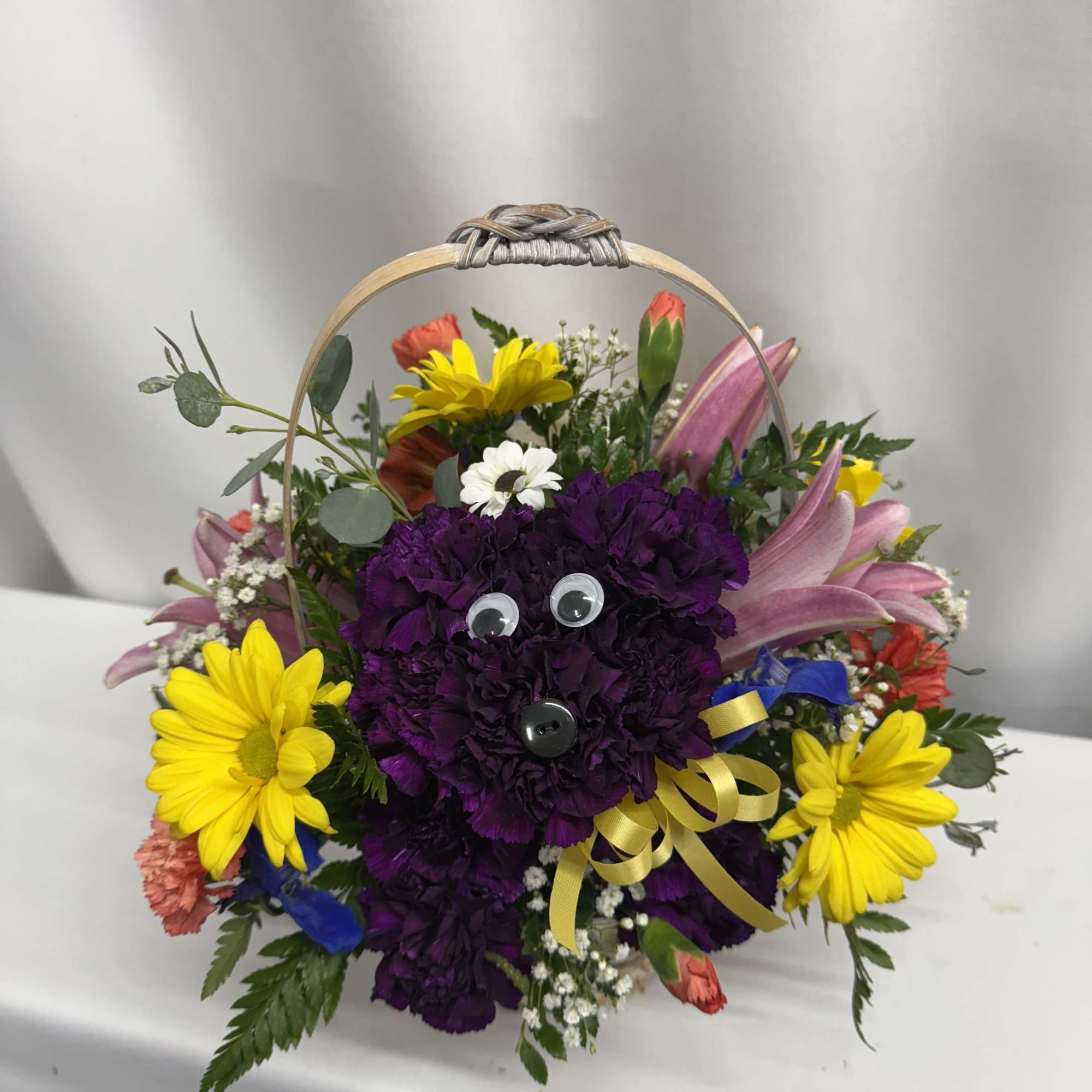 Basket arrangement with purple carnation dog face and bright flowers like yellow daisies and pink lilies