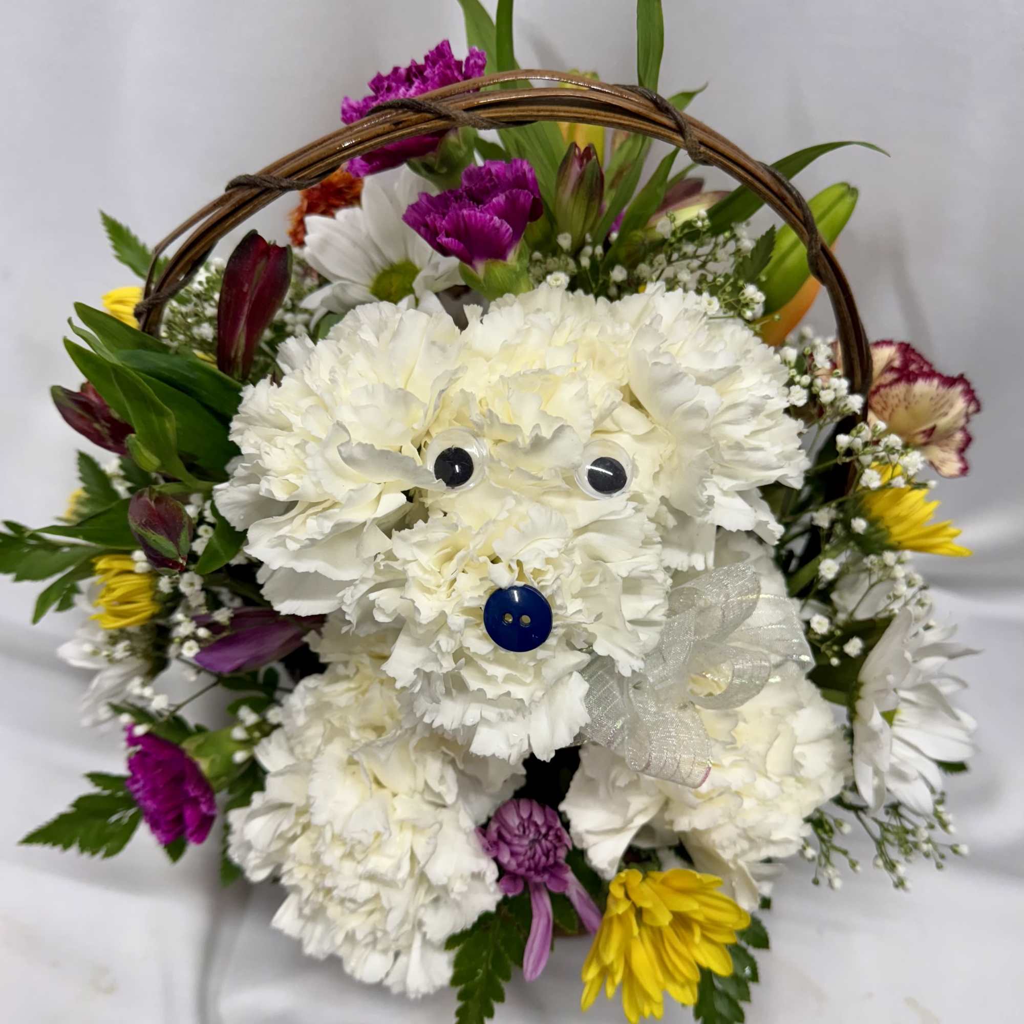 Basket arrangement with a white carnation dog, googly eyes, and bright mixed flowers around it.