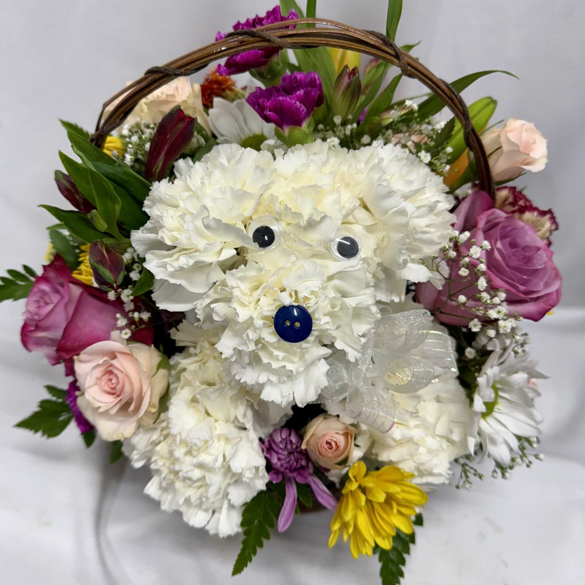 Basket arrangement with a white carnation dog figure surrounded by mixed pink, yellow, and purple flowers.