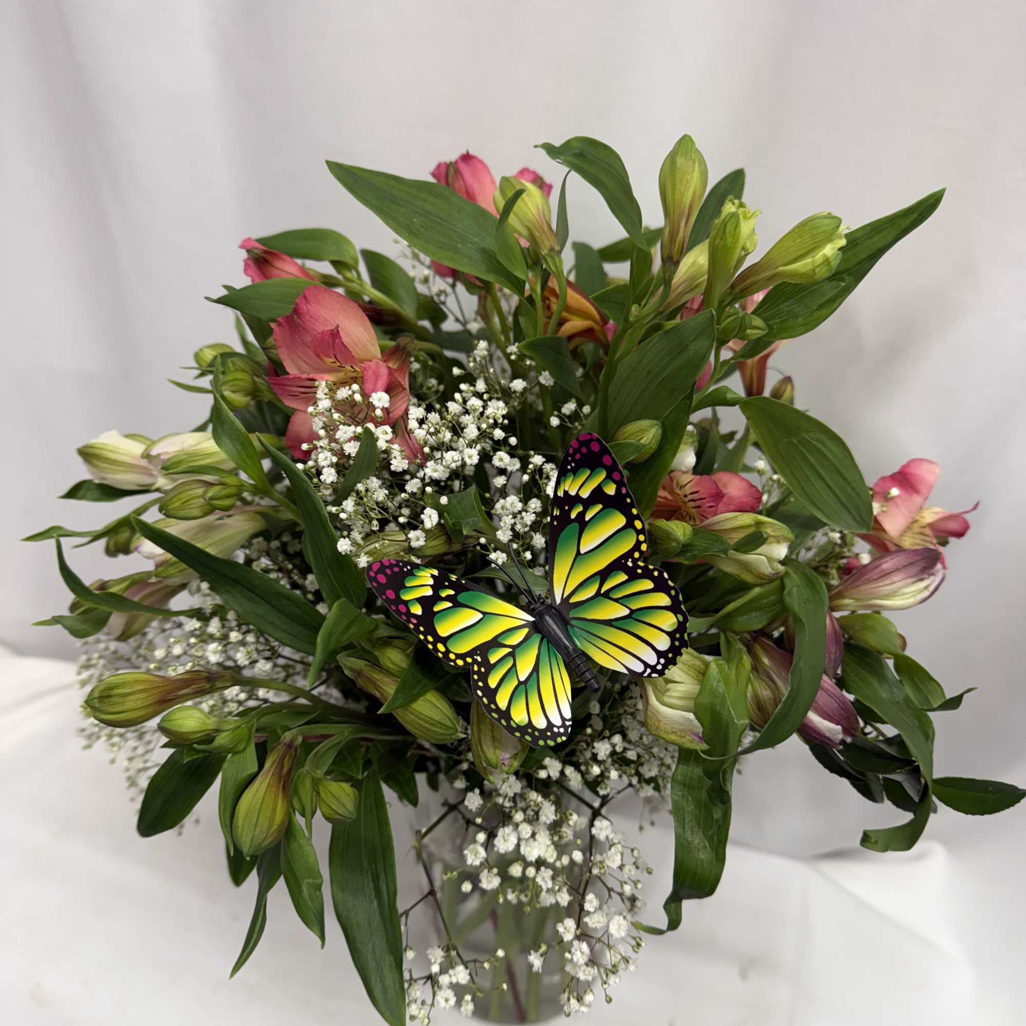Bouquet of pink alstroemeria with baby's breath and a butterfly pick in a glass vase
