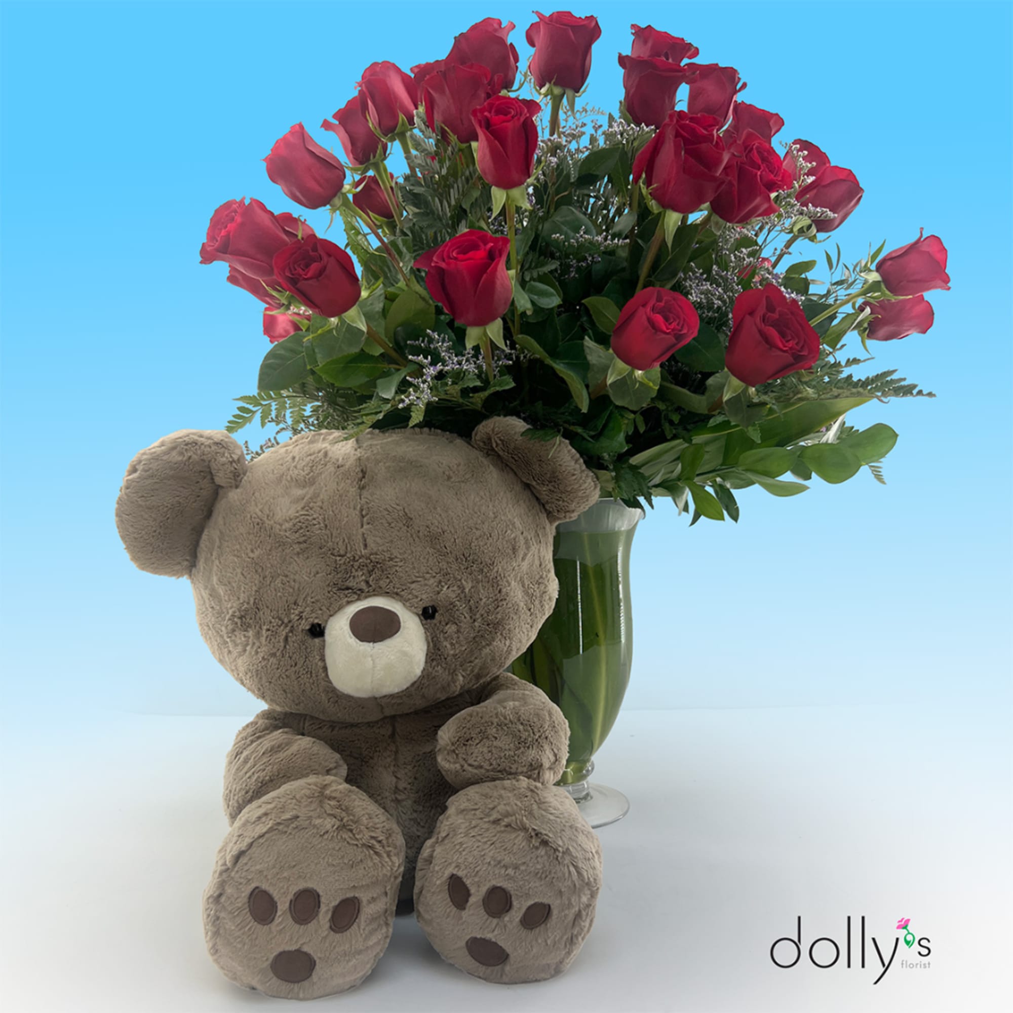 Red roses in a glass vase with a teddy bear in front