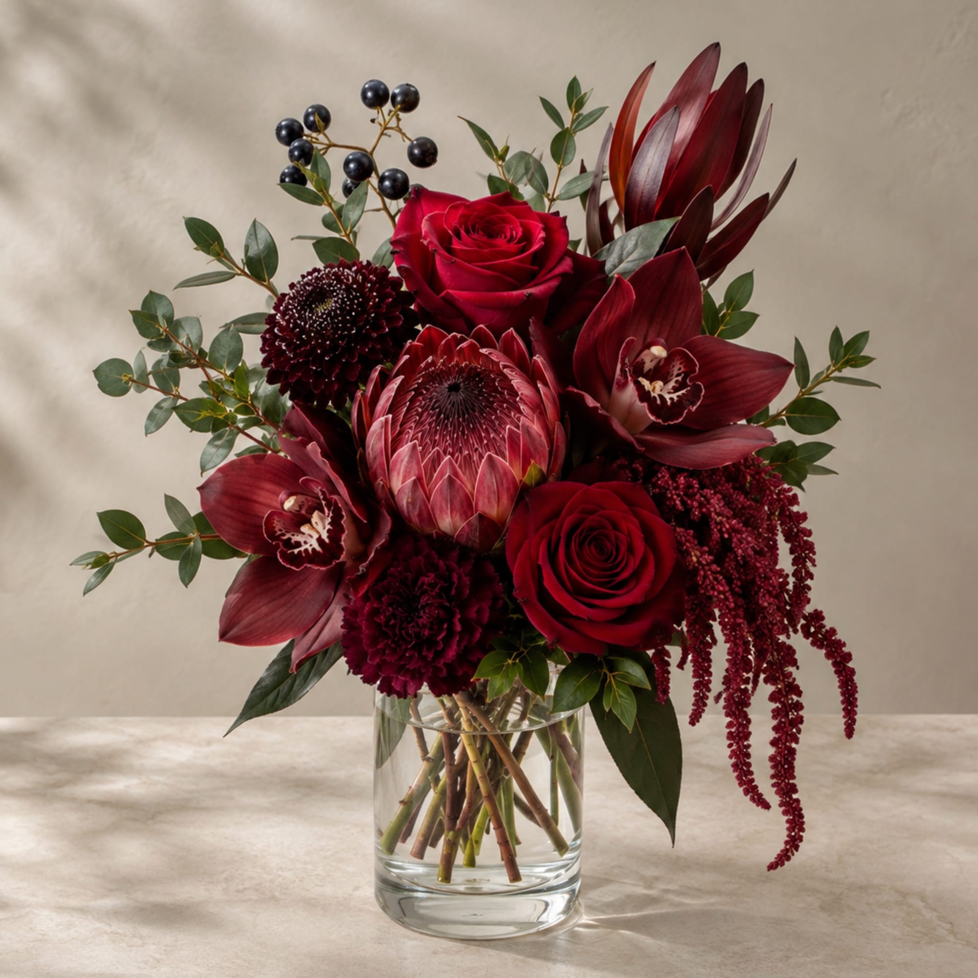 Deep red bouquet in a clear glass vase with roses and tropical blooms
