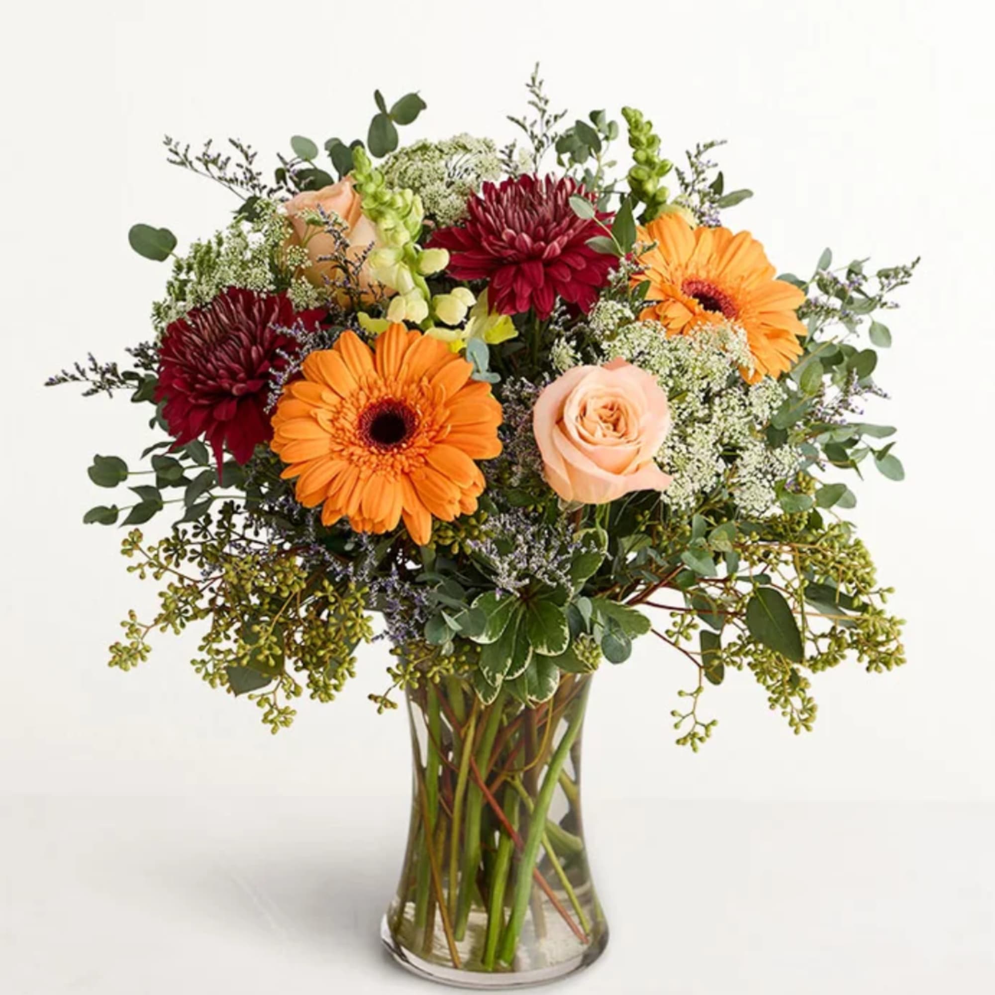 Mixed bouquet of orange gerbera daisies, burgundy mums, and peach roses in a glass vase