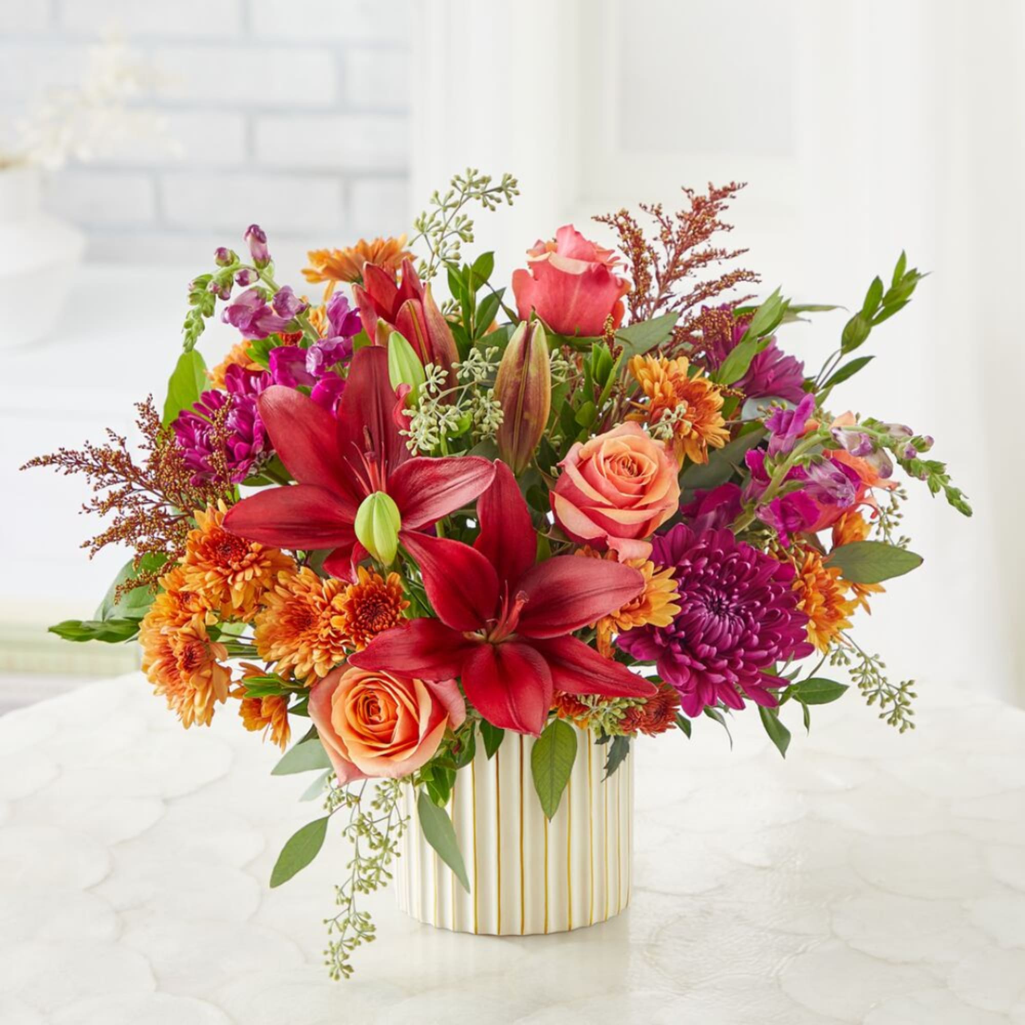 Mixed bouquet of red lilies, roses, and orange chrysanthemums in a striped vase
