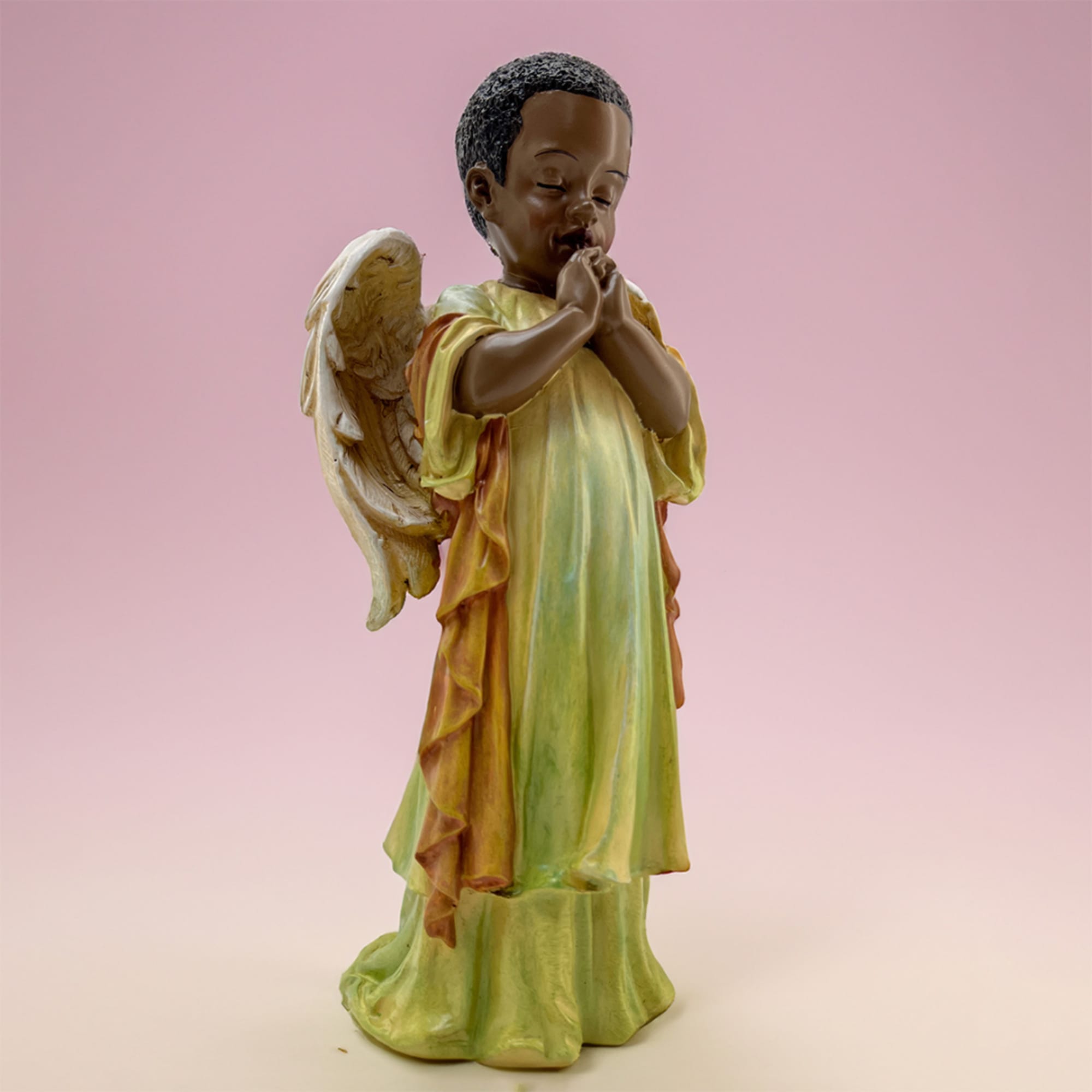 Decorative angel figurine with folded hands on a pink background