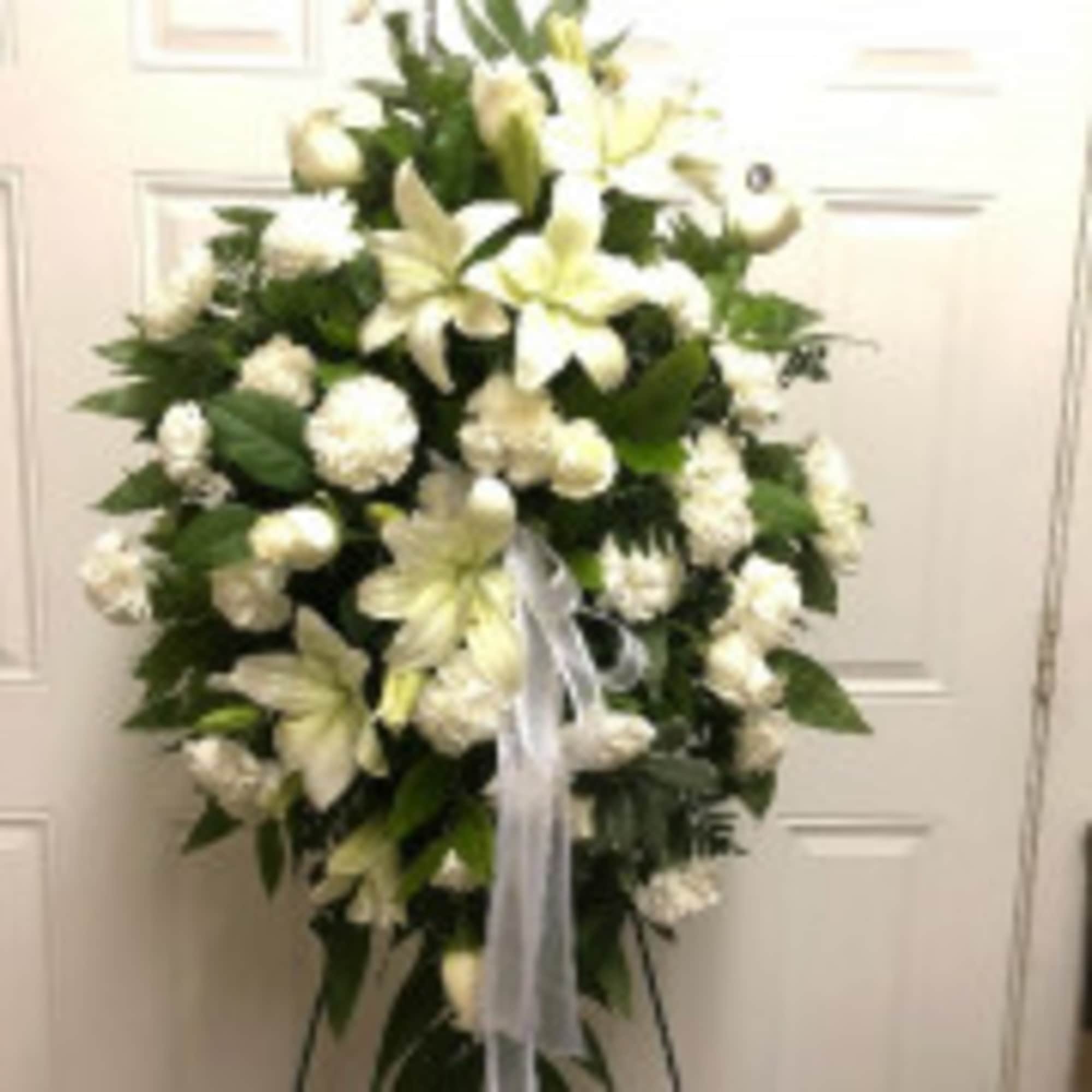 White floral standing spray with lilies and carnations on a ribboned easel