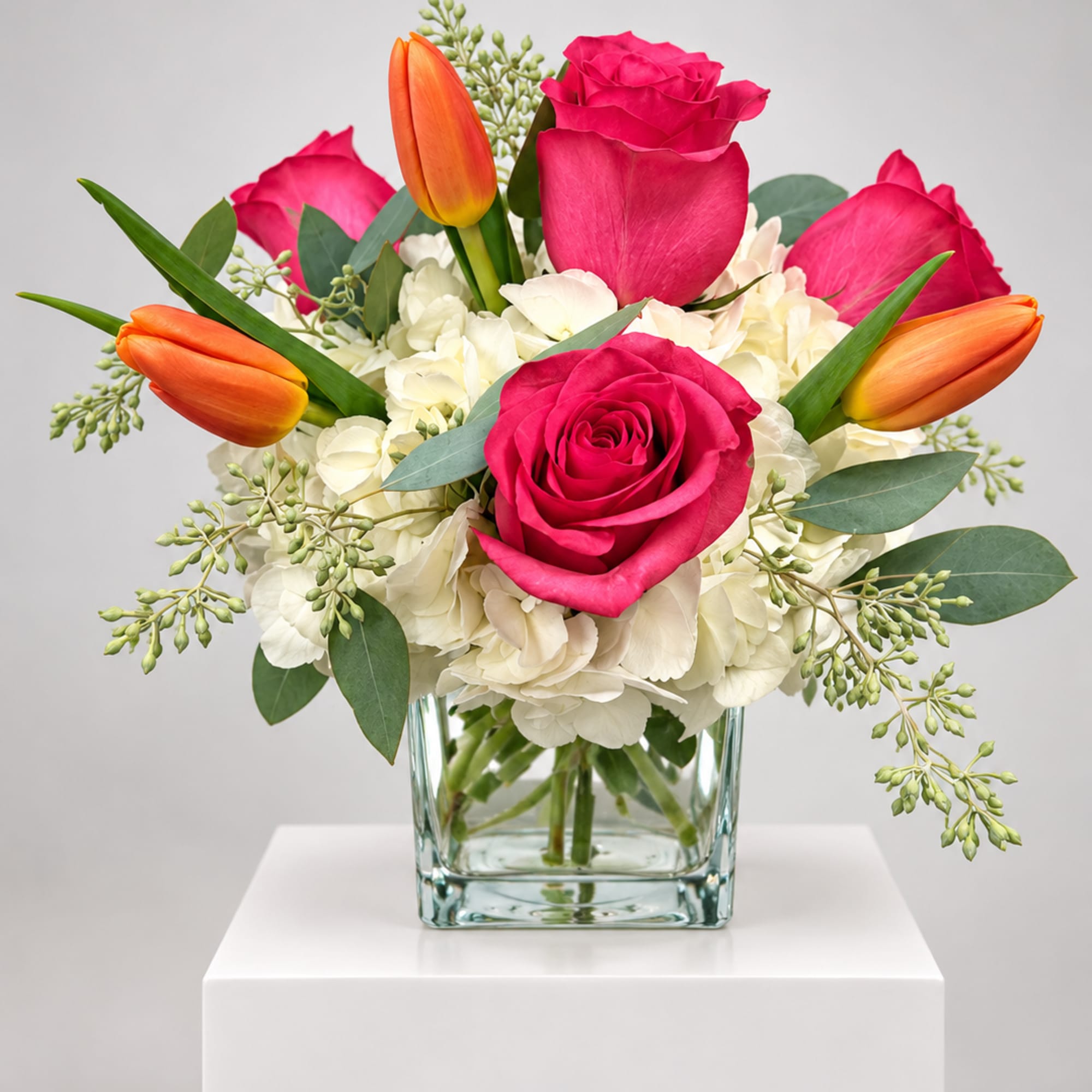 Pink roses and orange tulips in a clear glass vase