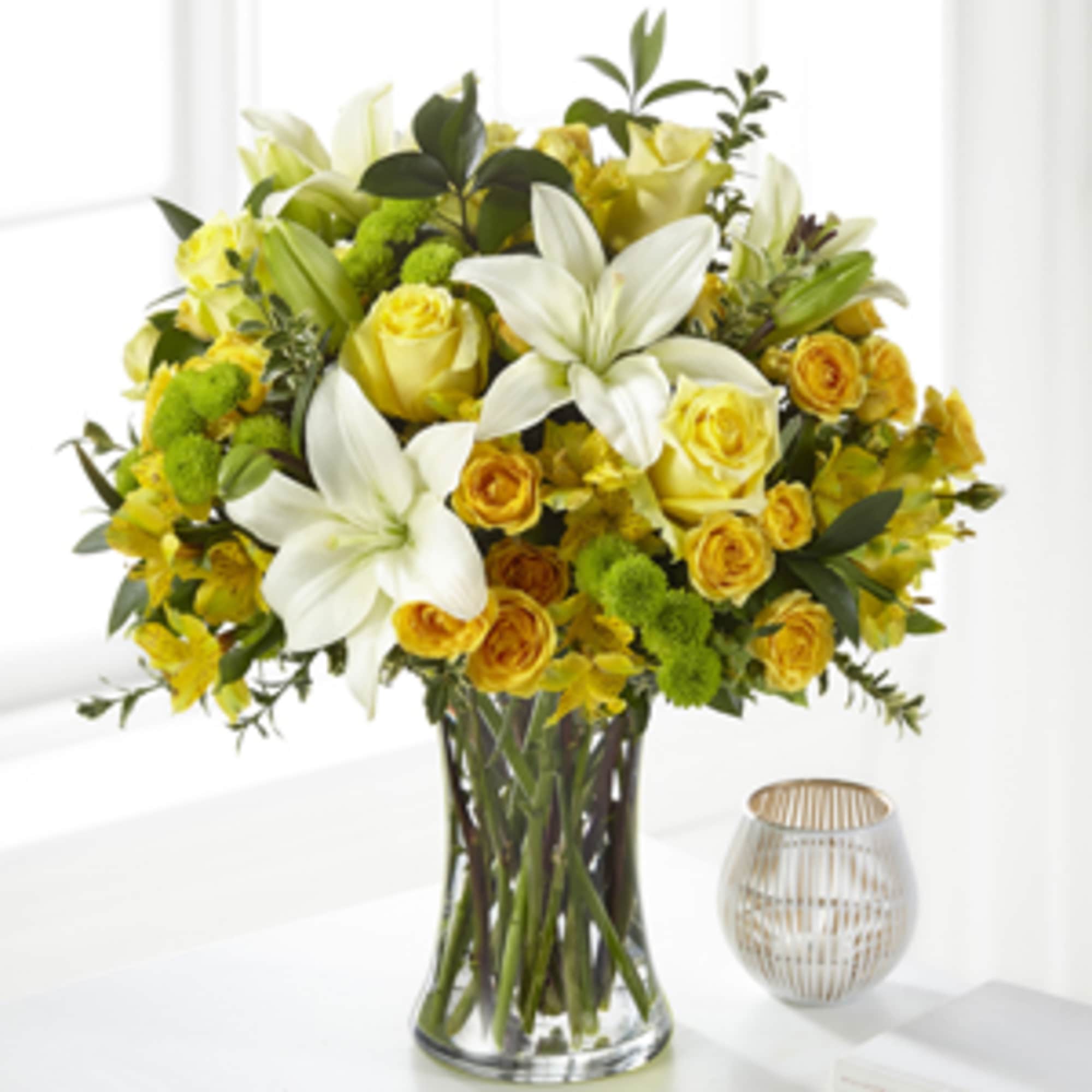Yellow and white bouquet with lilies and roses in a clear glass vase