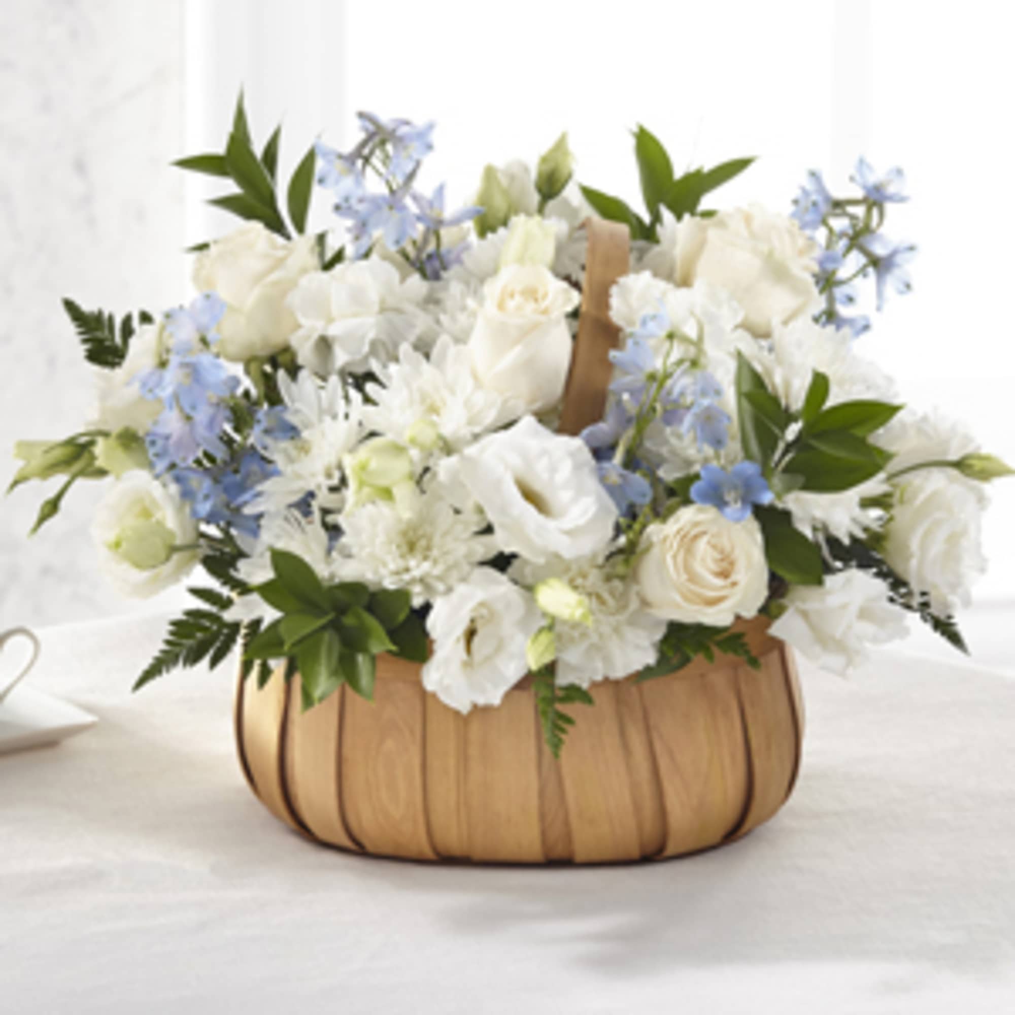 White roses and blue flowers arranged in a wooden basket