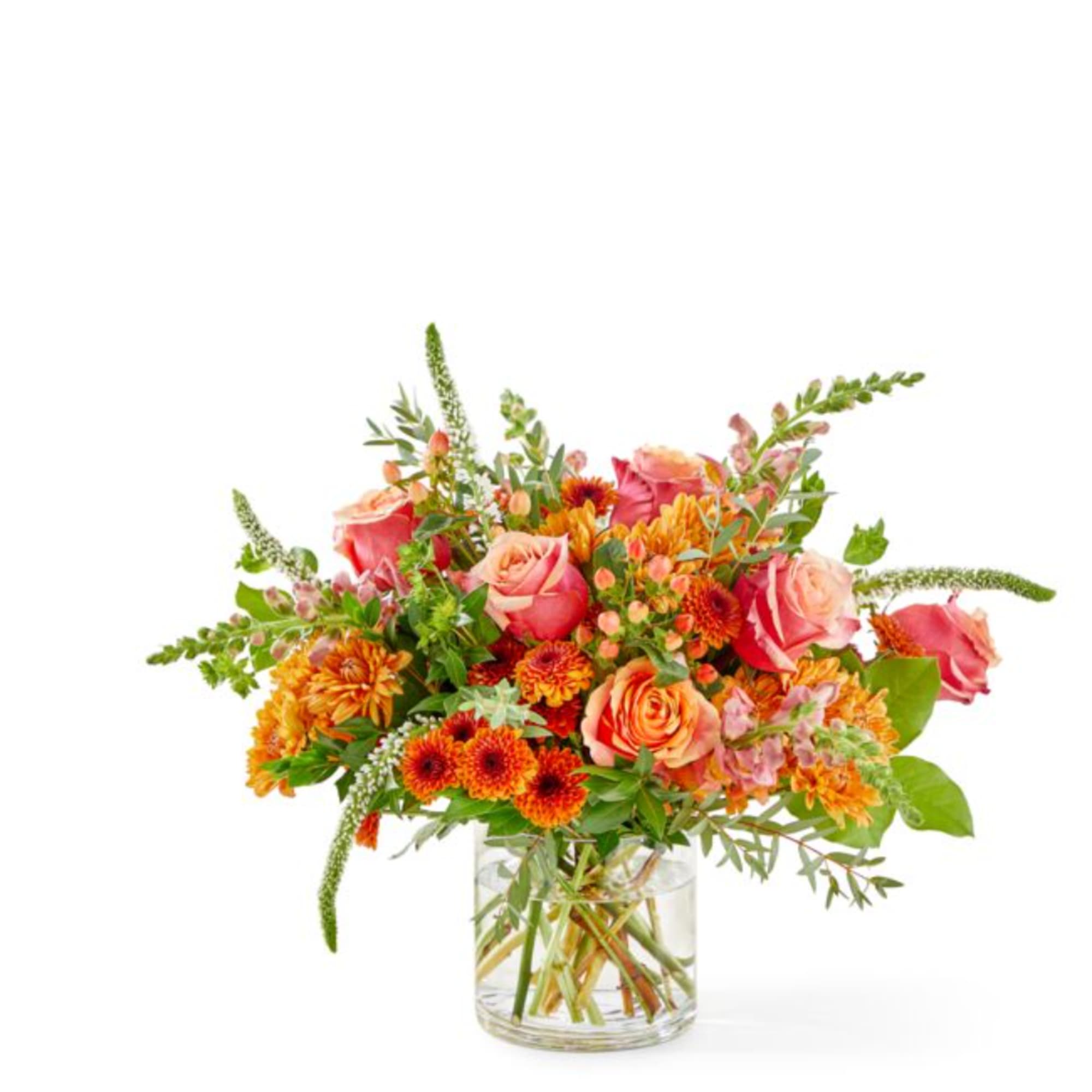 Mixed bouquet of pink roses and orange flowers in a clear glass vase