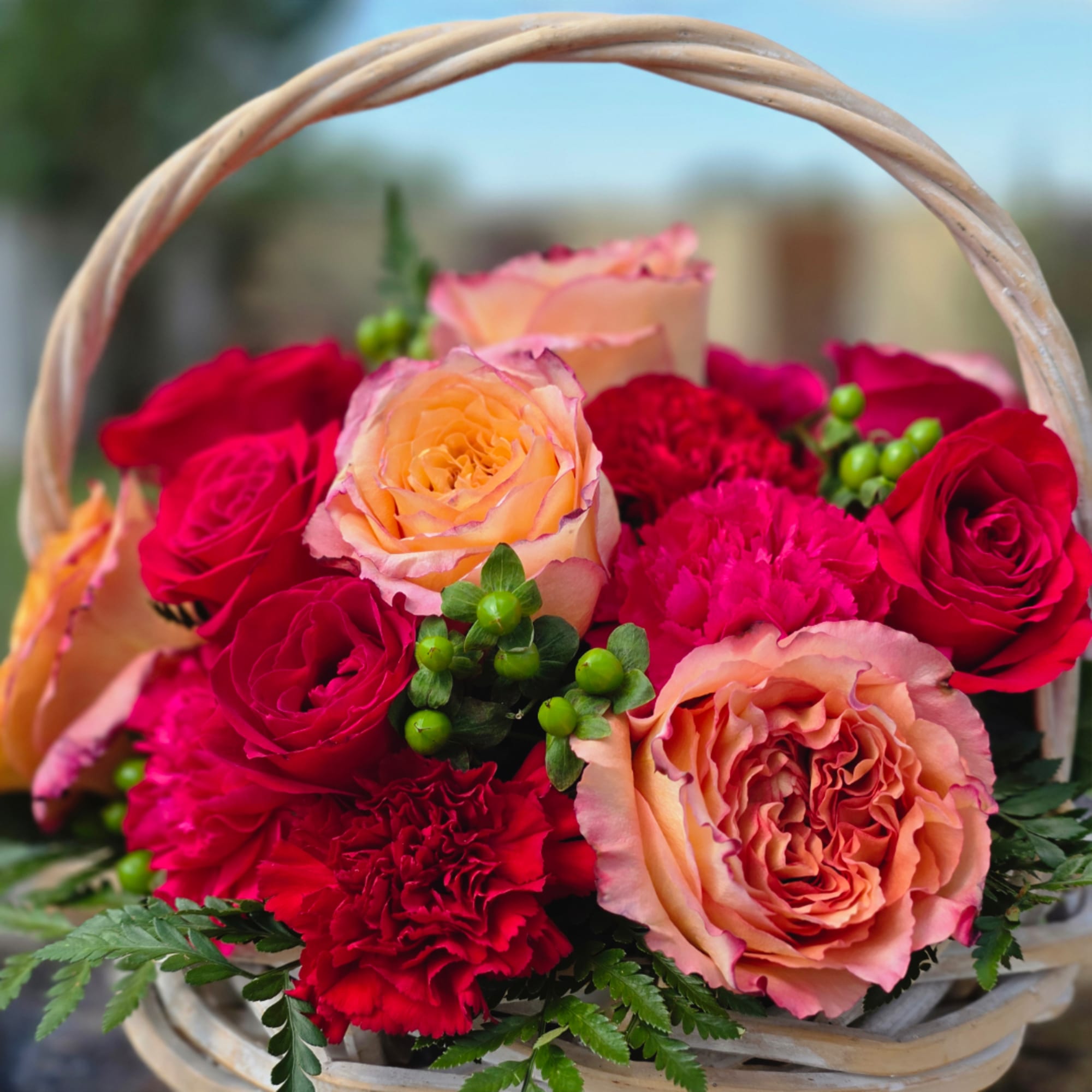 Basket of pink and peach roses with red carnations