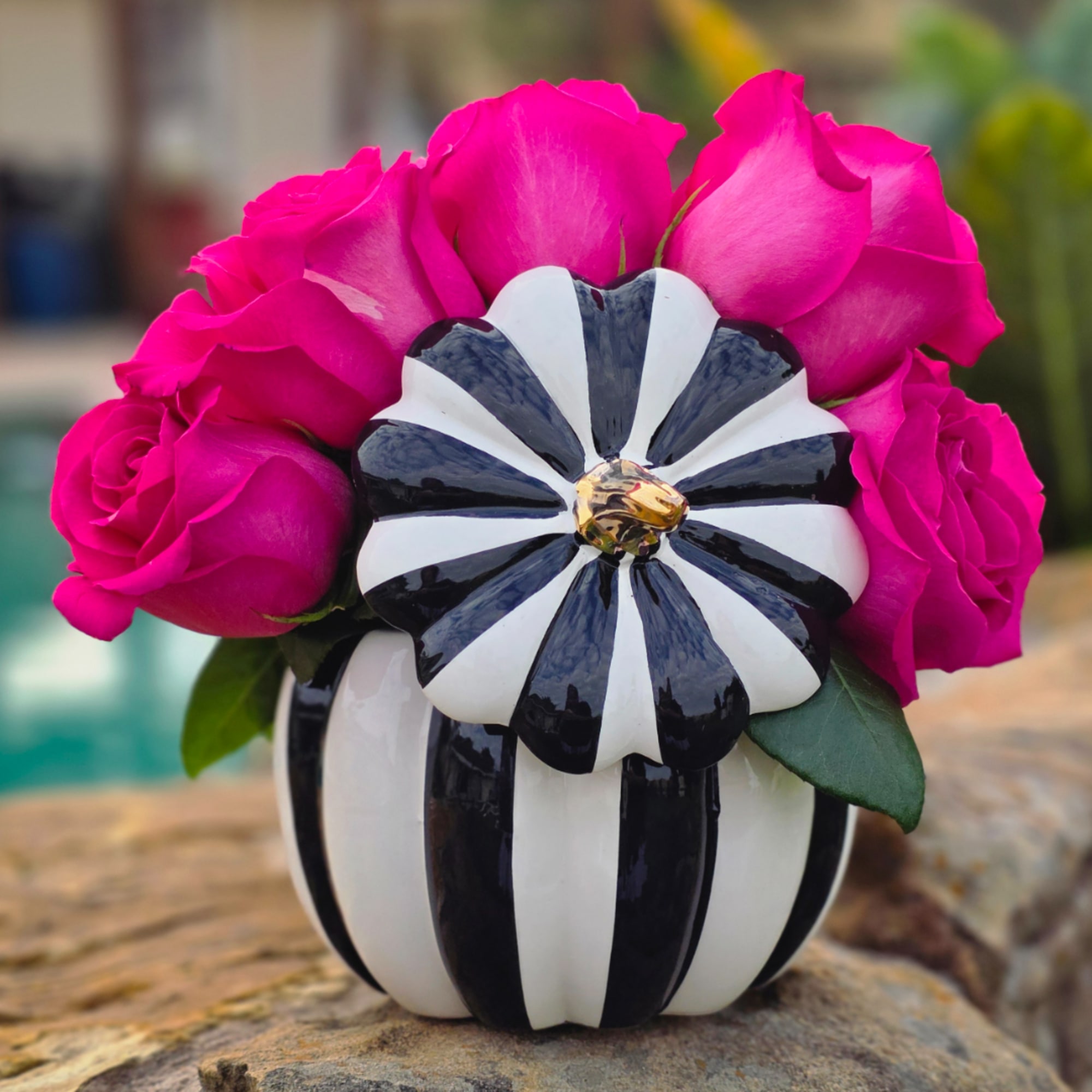 Pink roses arranged in a black-and-white striped vase with a decorative flower accent
