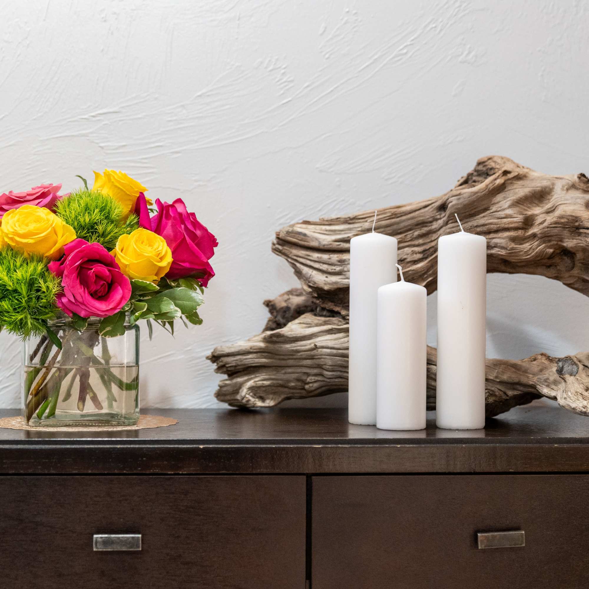 Pink and yellow roses in a glass vase beside white pillar candles