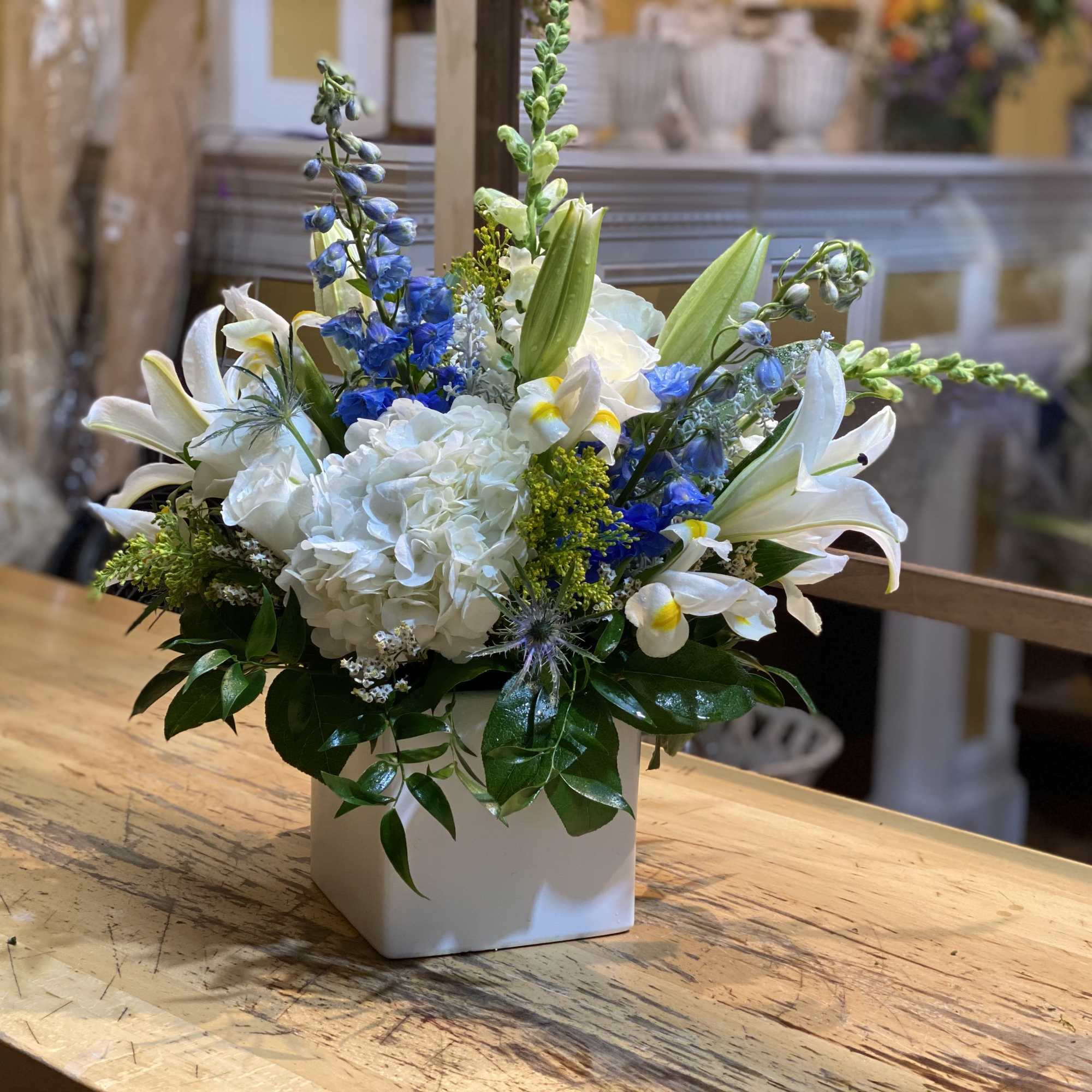 White and blue floral arrangement in a square white vase