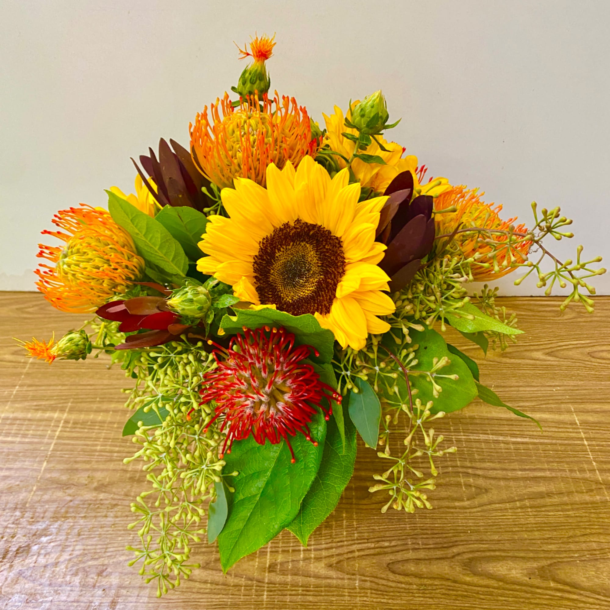 Sunflower bouquet with orange and red pincushion blooms on a wooden surface