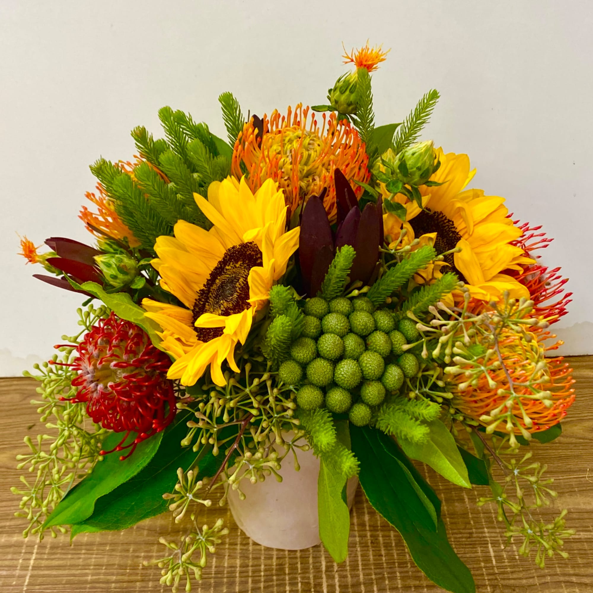 Bright sunflower and protea arrangement in a white vase