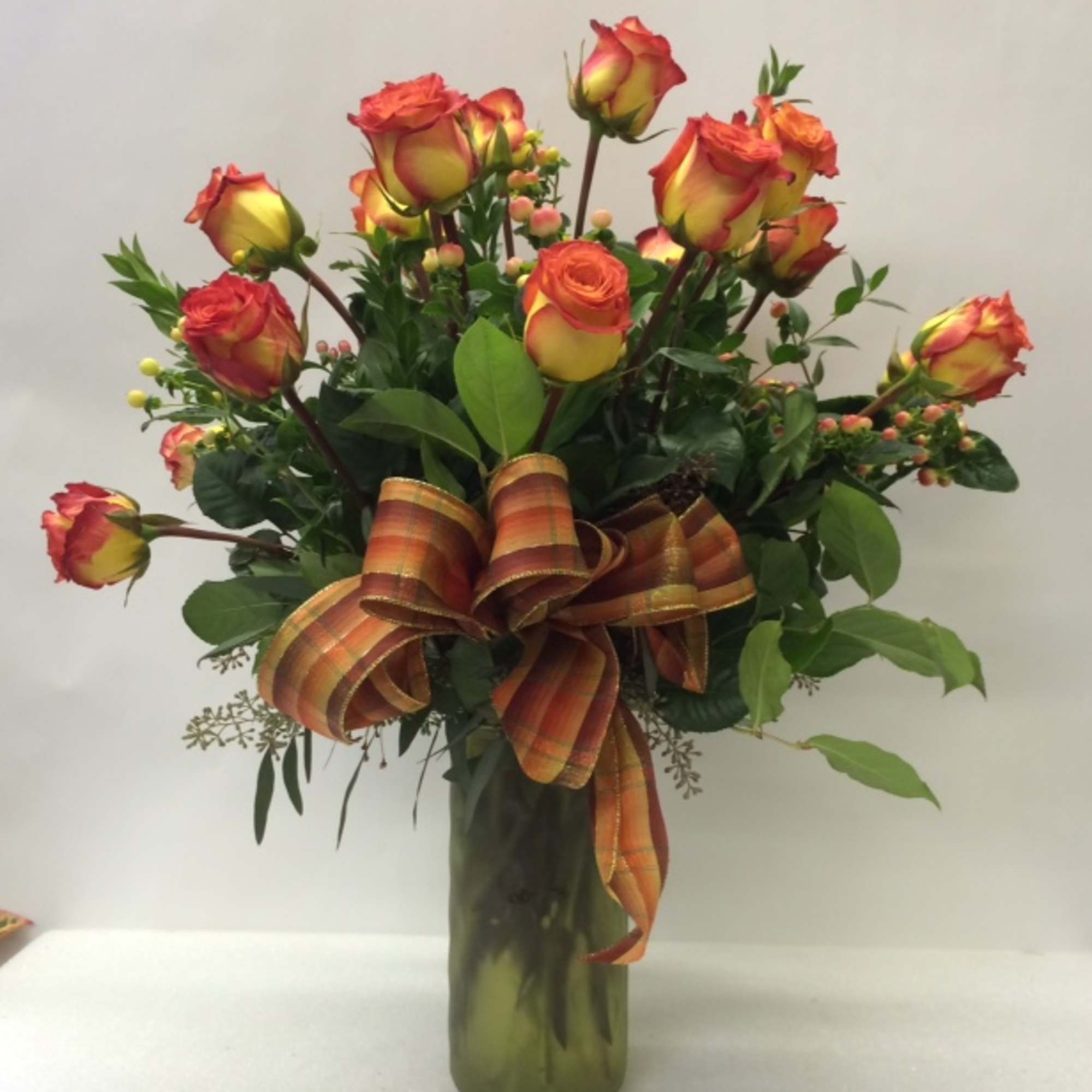 Orange-yellow roses in a tall glass vase with a striped ribbon