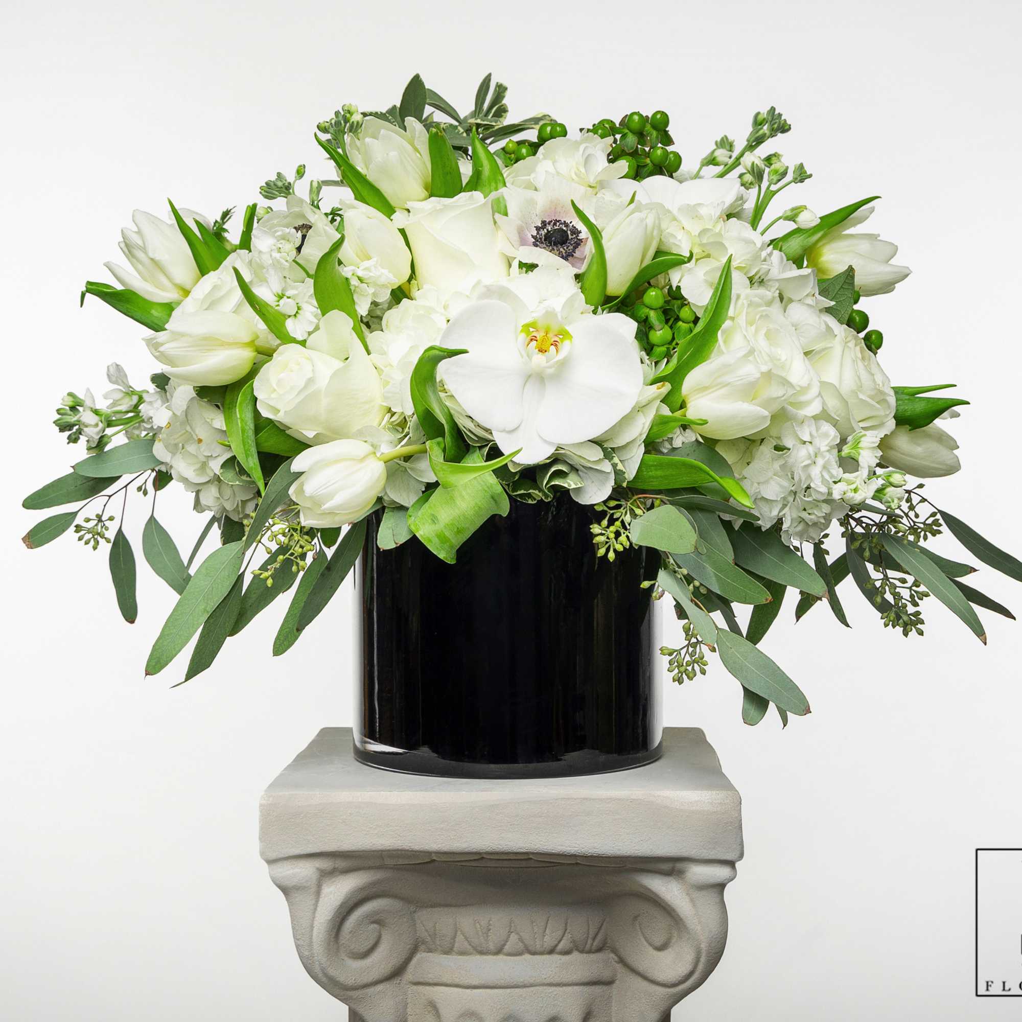 White floral arrangement in a black vase with trailing greenery