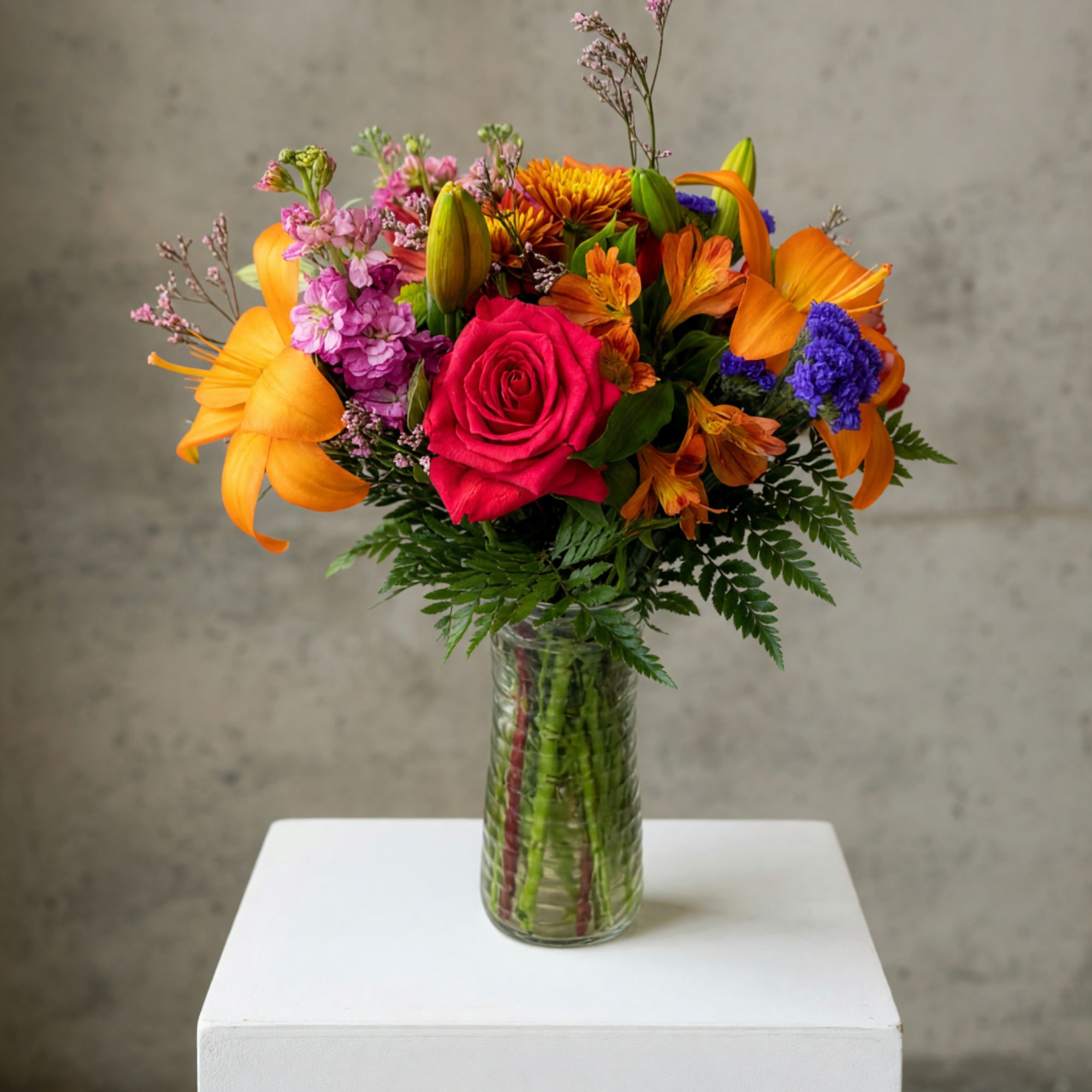 Mixed bouquet of roses, lilies, and orange blooms in a glass vase