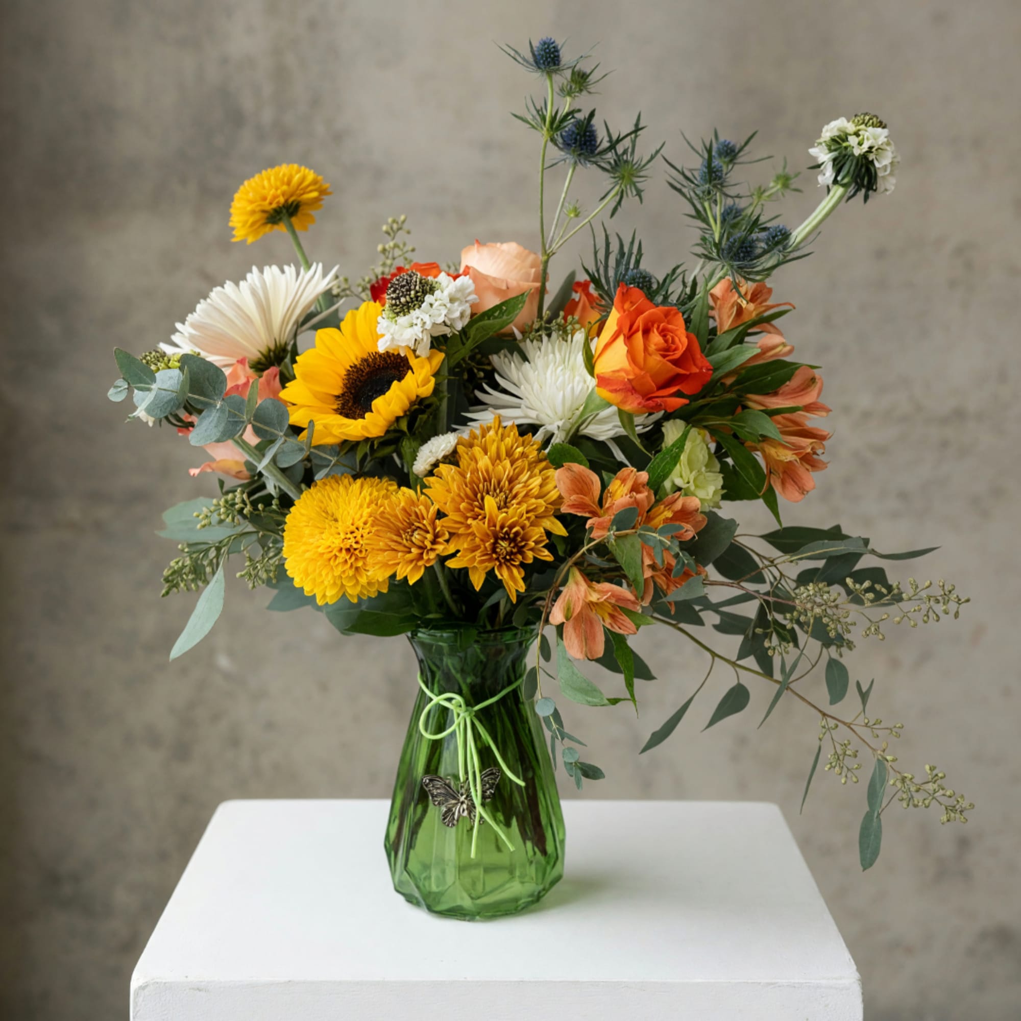 Mixed bouquet of sunflowers, roses, and chrysanthemums in a green glass vase