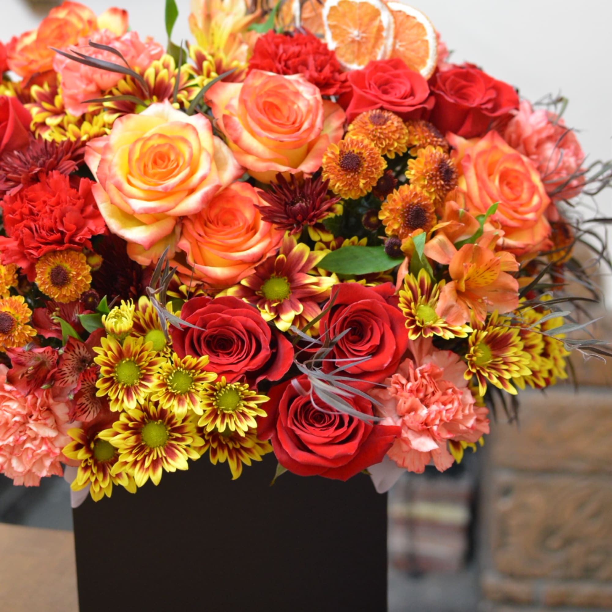 Mixed bouquet of red and peach roses with orange chrysanthemums in a black box