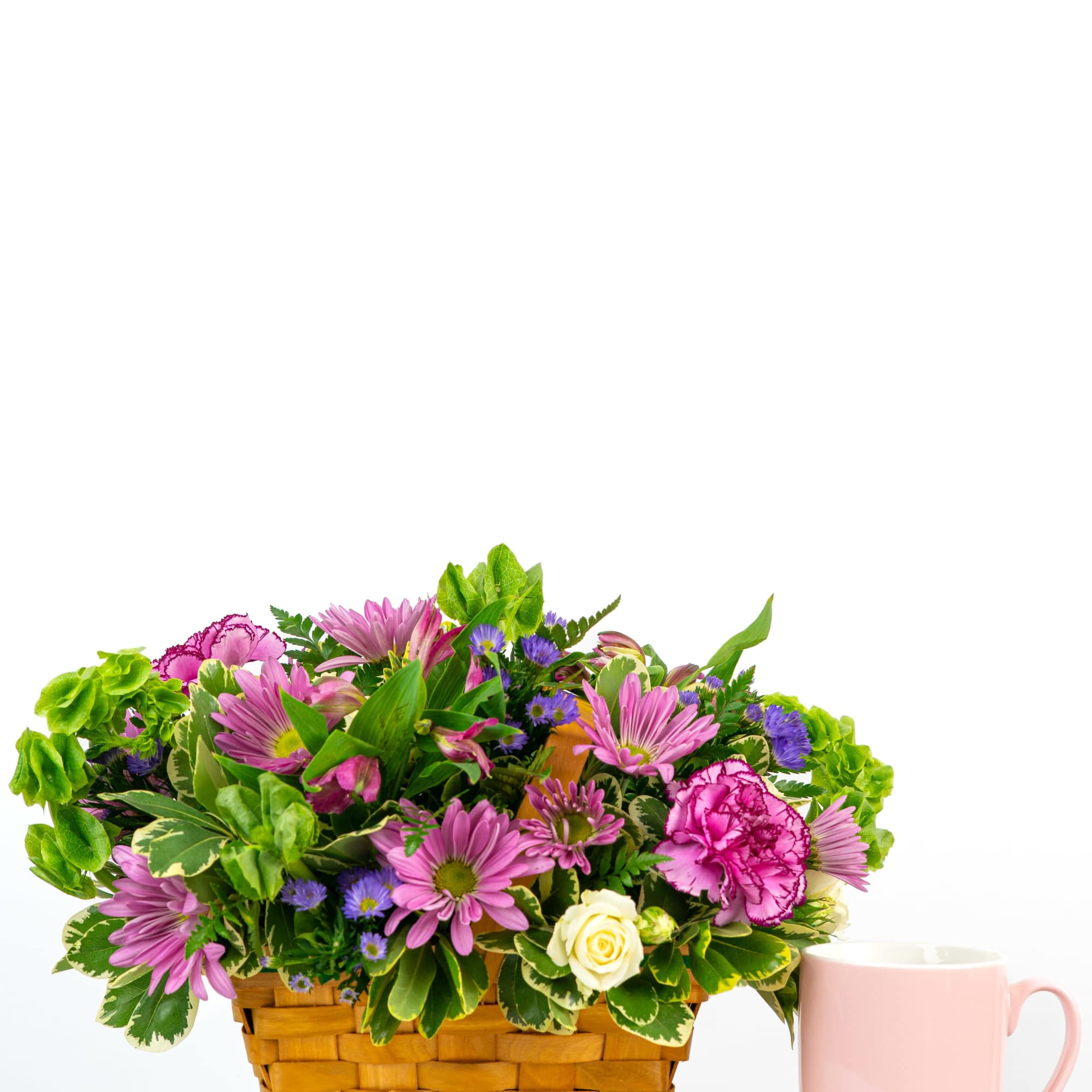 Low basket of pink daisies, purple asters, carnations and a white rose beside a pink mug