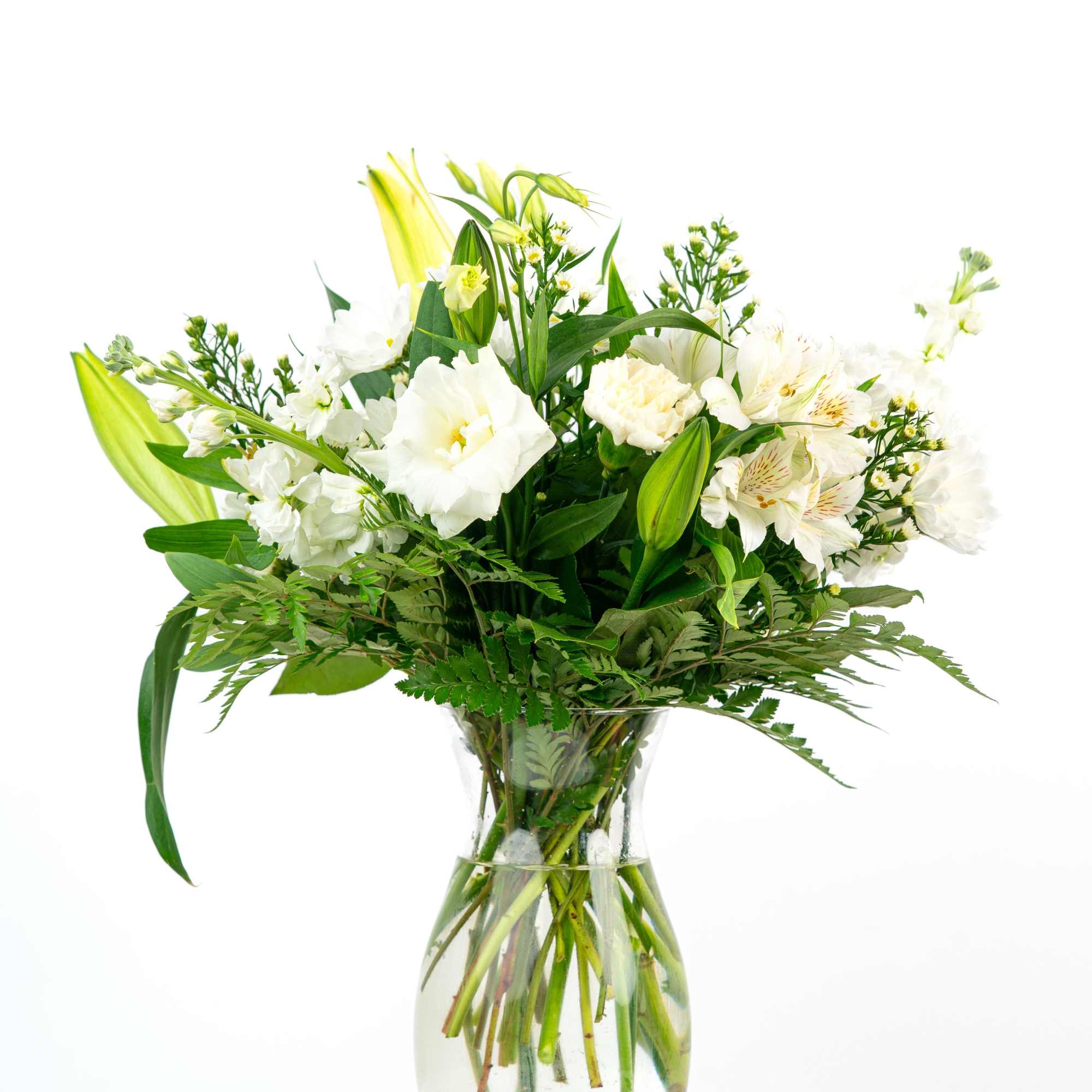 Tall arrangement of white lilies, lisianthus, and other blooms in a clear glass vase.