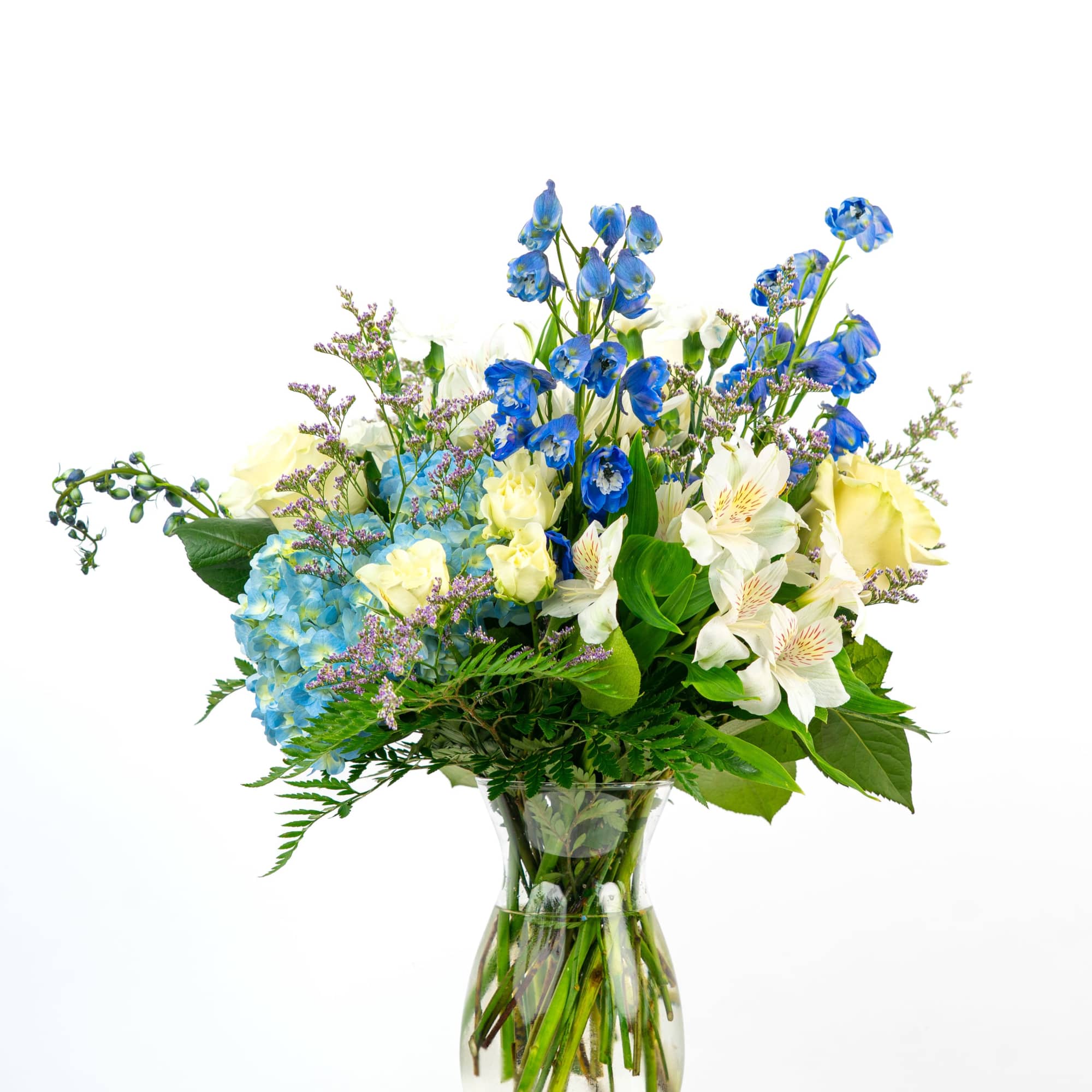 Tall mixed bouquet of blue hydrangea, blue delphinium, yellow roses, and white alstroemeria in a clear glass vase