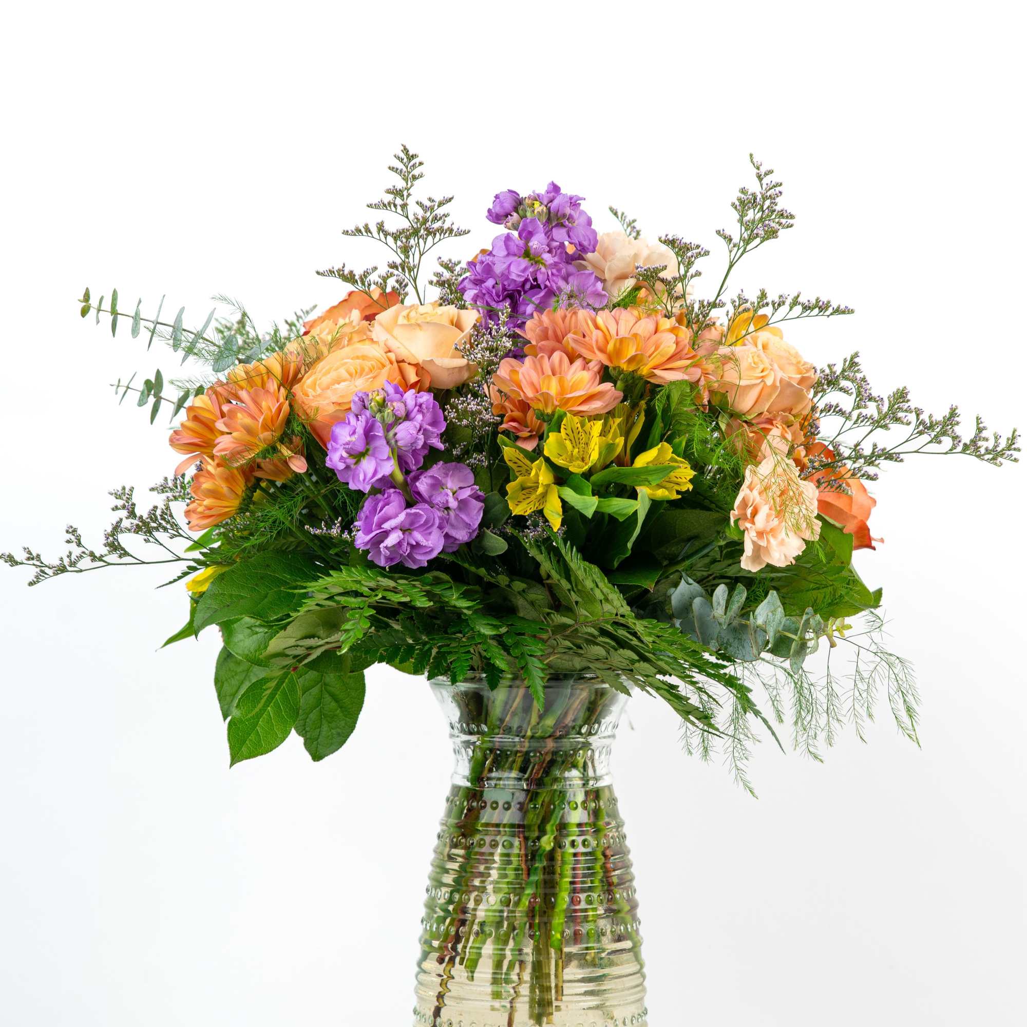 Mixed bouquet of orange, purple, and yellow flowers in a glass vase