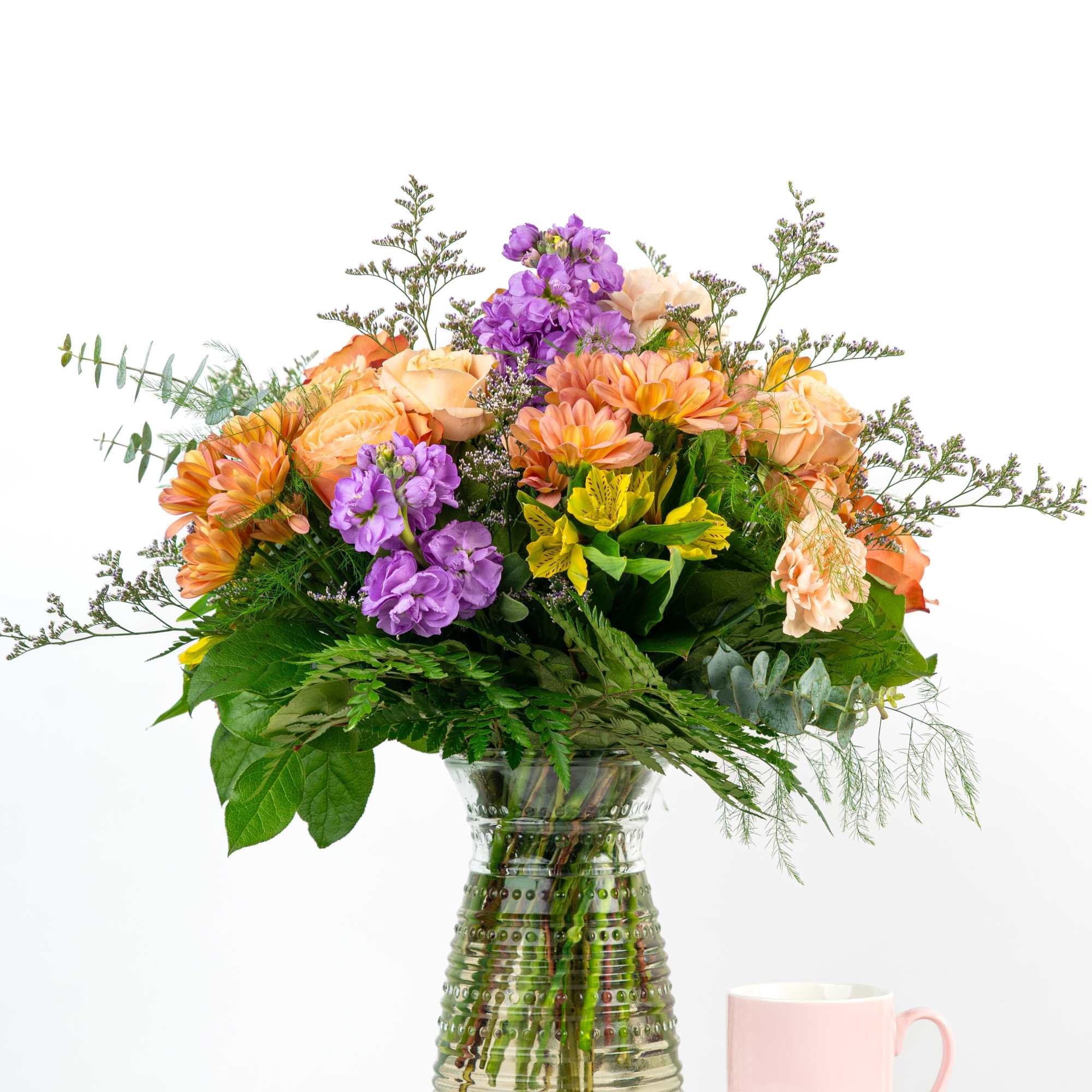 Mixed bouquet of orange, purple, and peach flowers in a glass vase