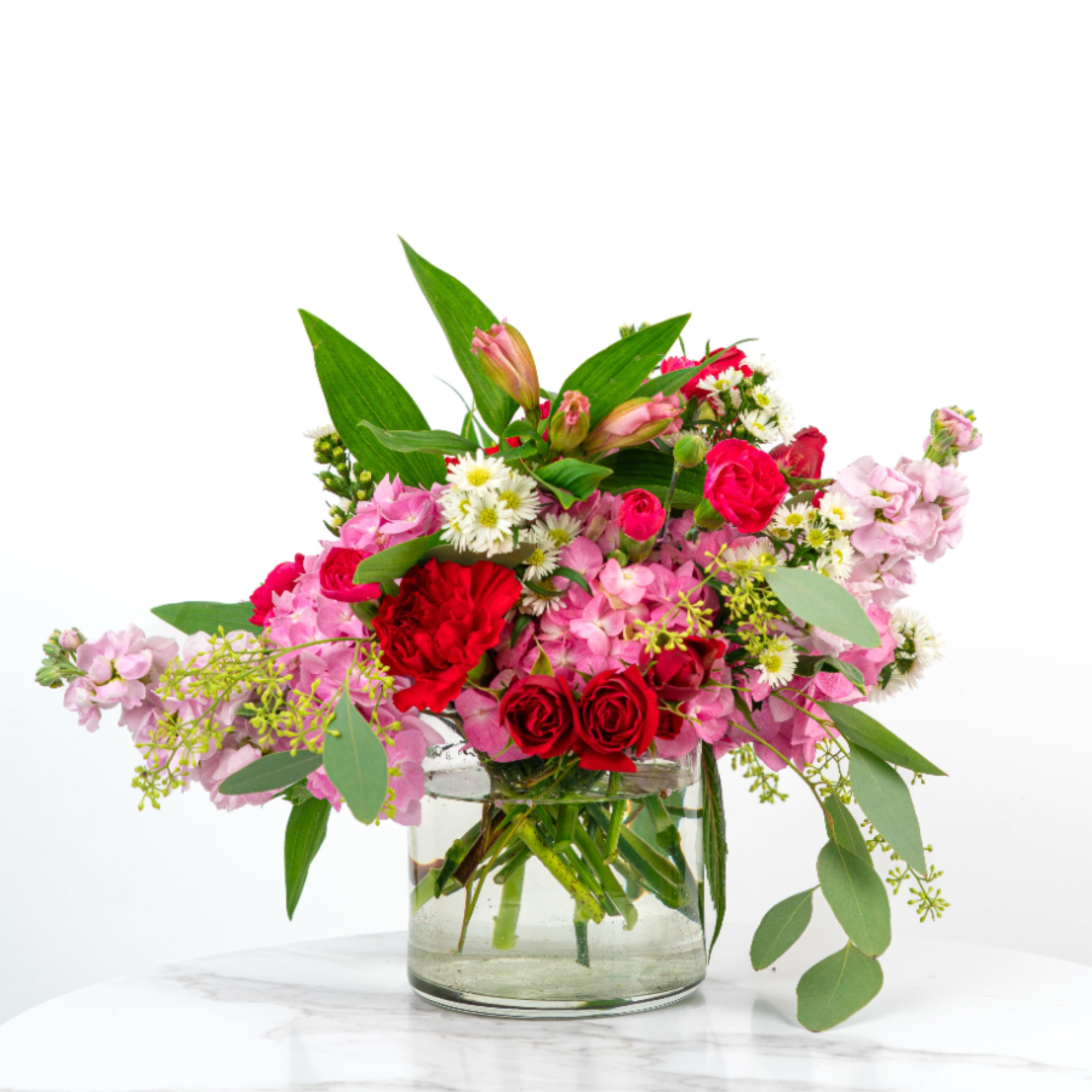 Low glass vase with red roses, carnations, pink blooms, and small white daisies in a mixed arrangement