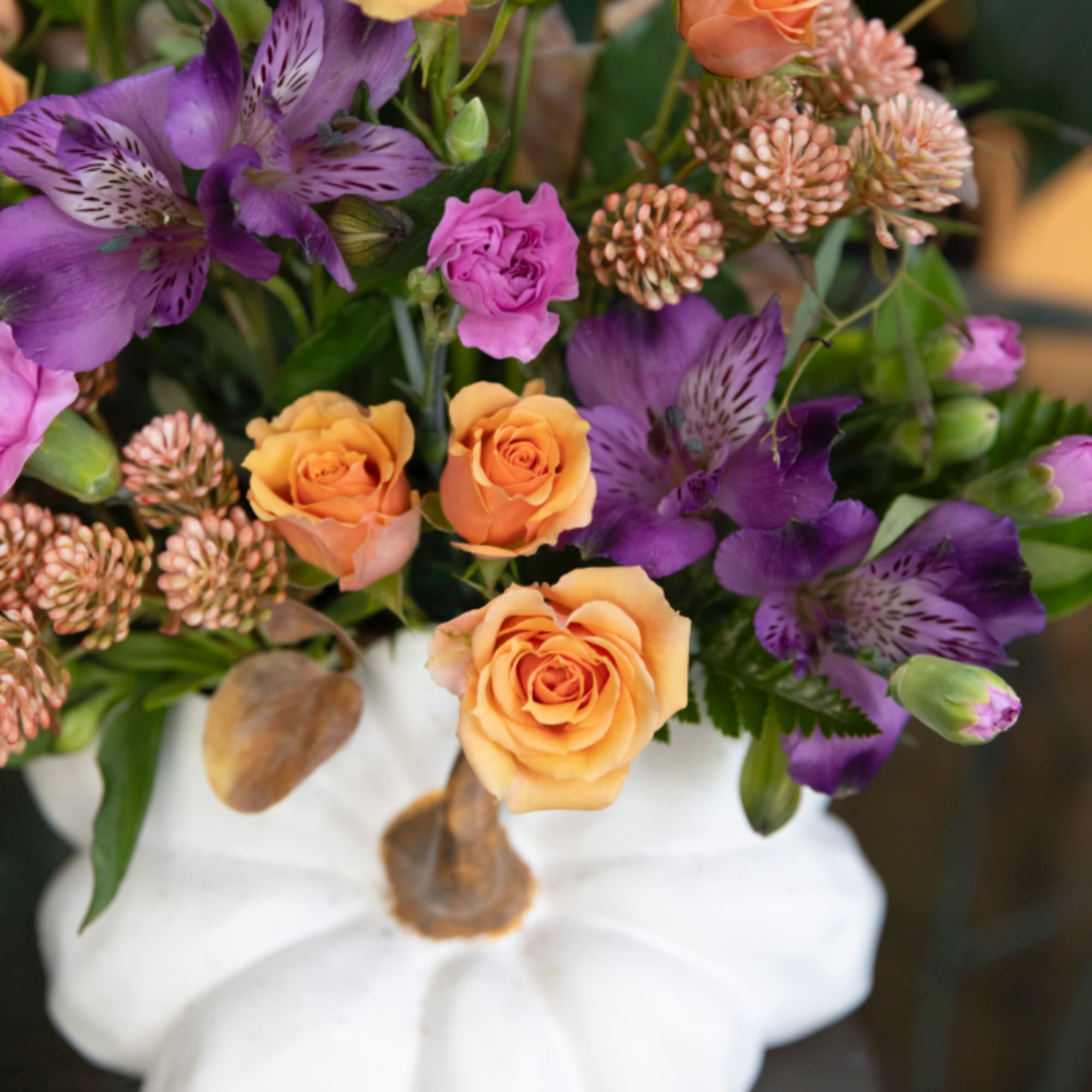 Bouquet of purple alstroemeria and orange roses in a white pumpkin vase