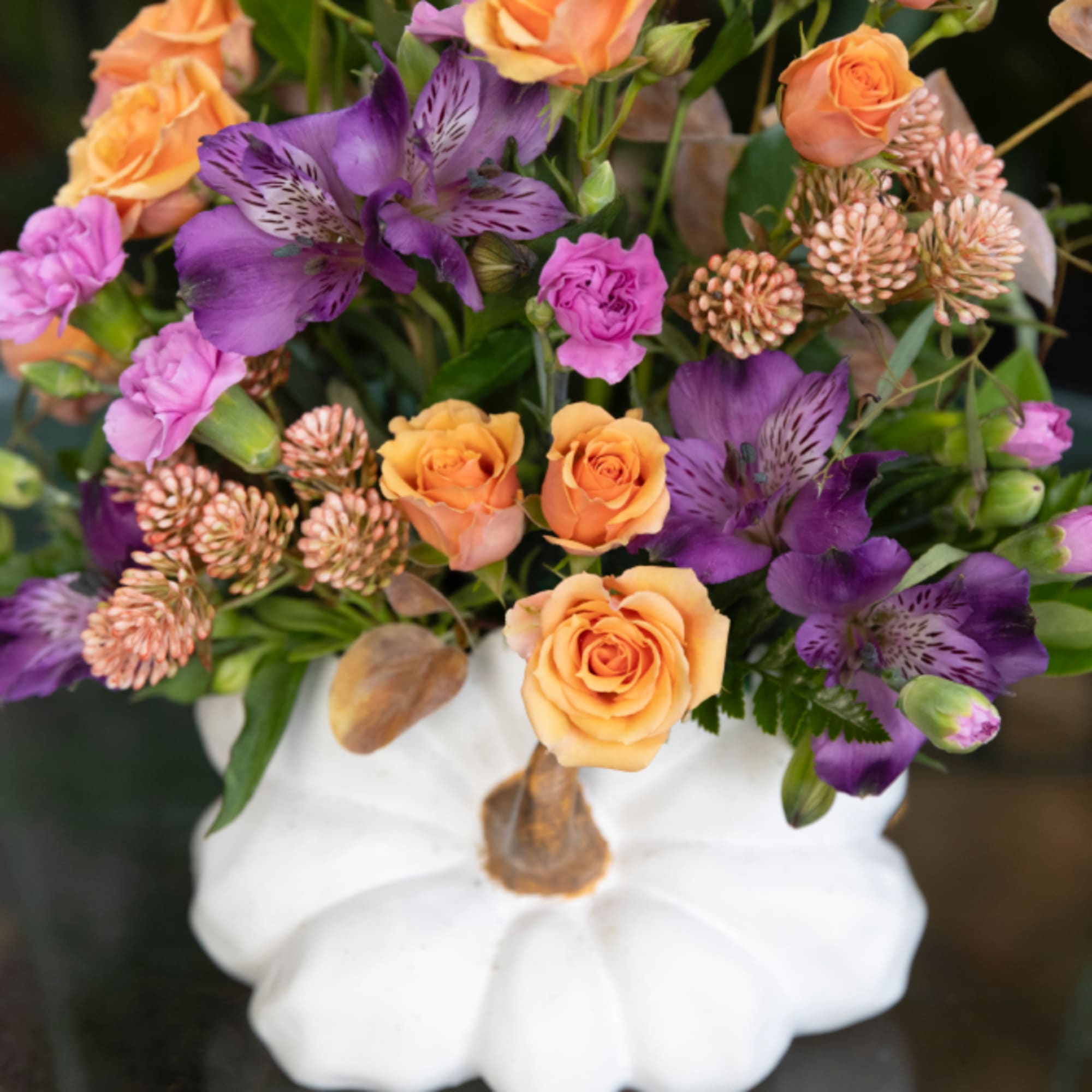 Orange roses and purple flowers arranged in a white pumpkin vase