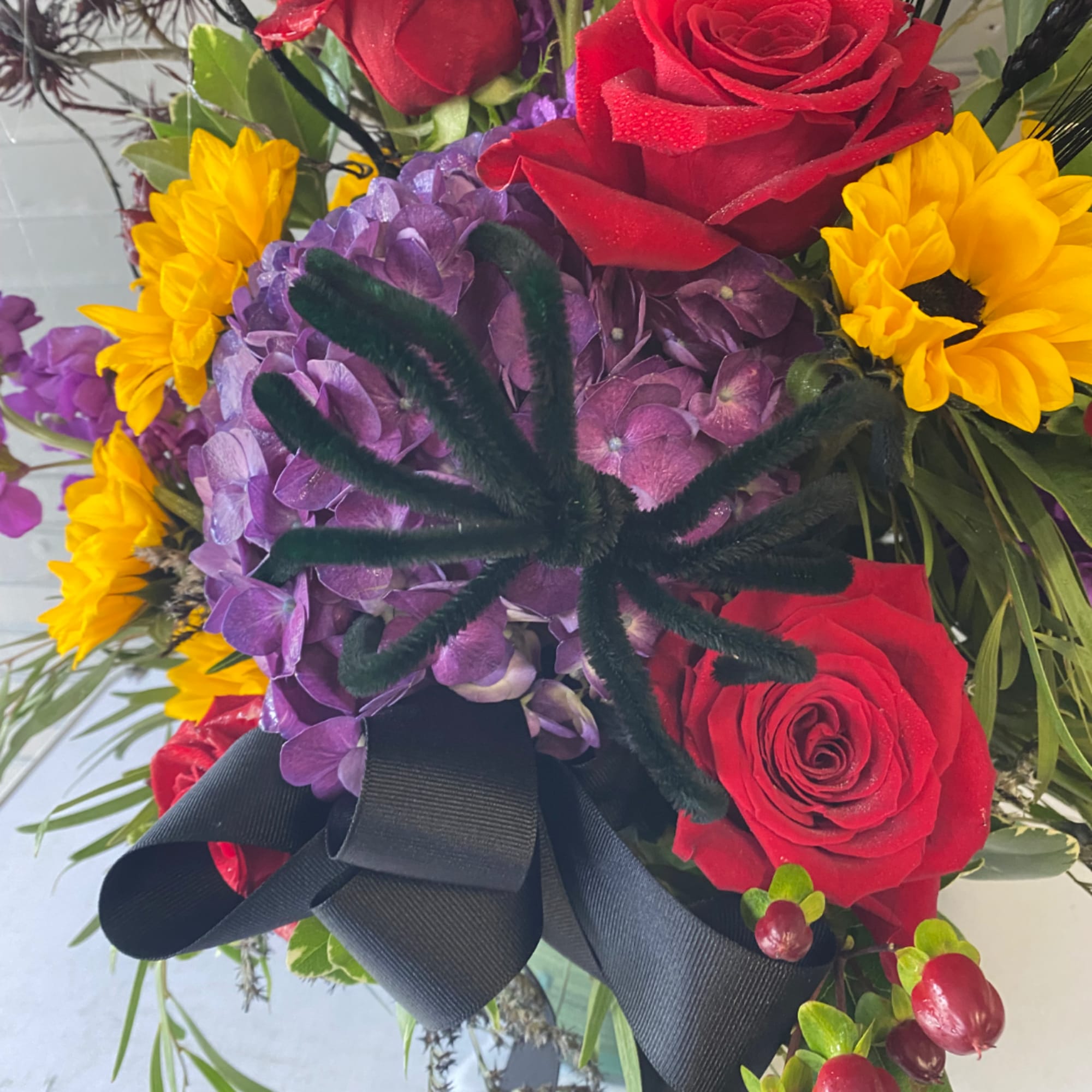 Bouquet of red roses, purple hydrangea, and yellow sunflowers with a black ribbon
