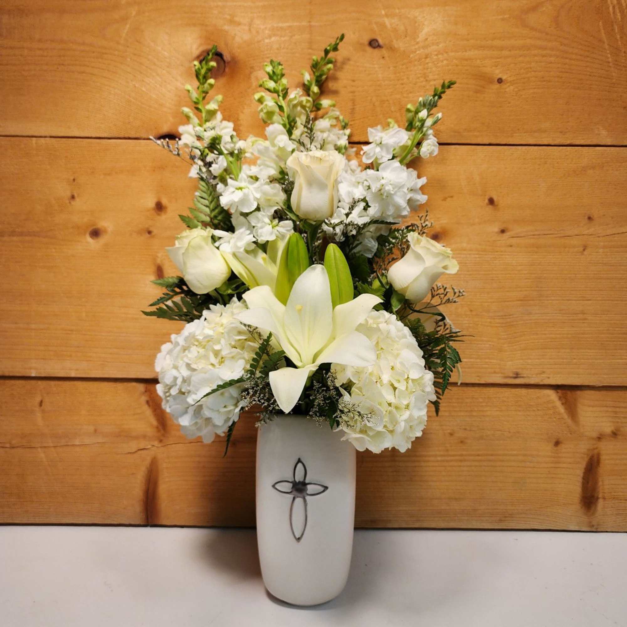 White floral arrangement in a white vase with a cross emblem