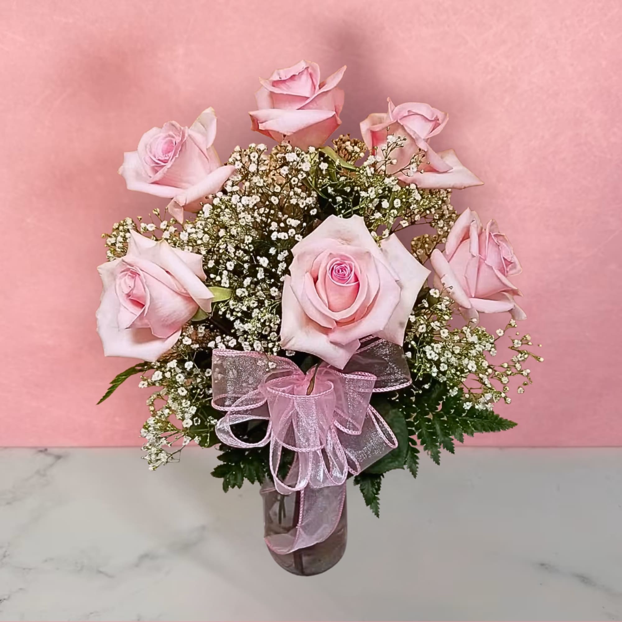 Pink roses arranged in a glass vase with baby's breath and a pink ribbon